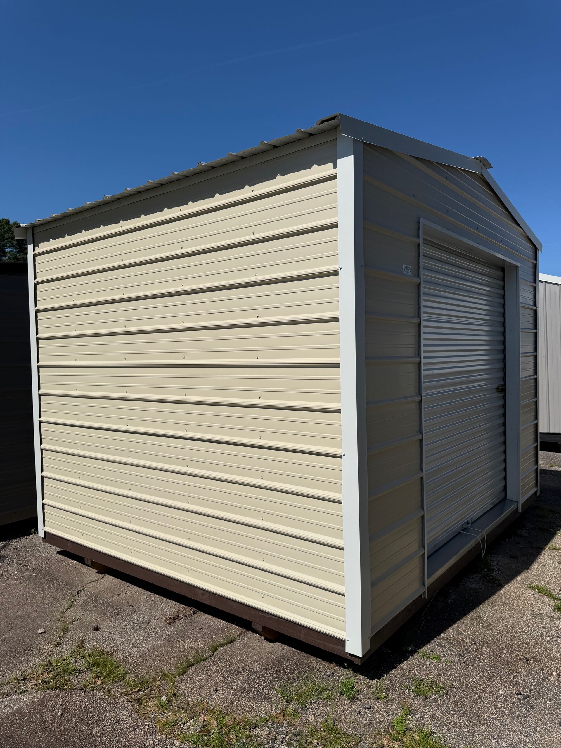 Beige metal shed with a roll-up door, shown outdoors on a sunny day.