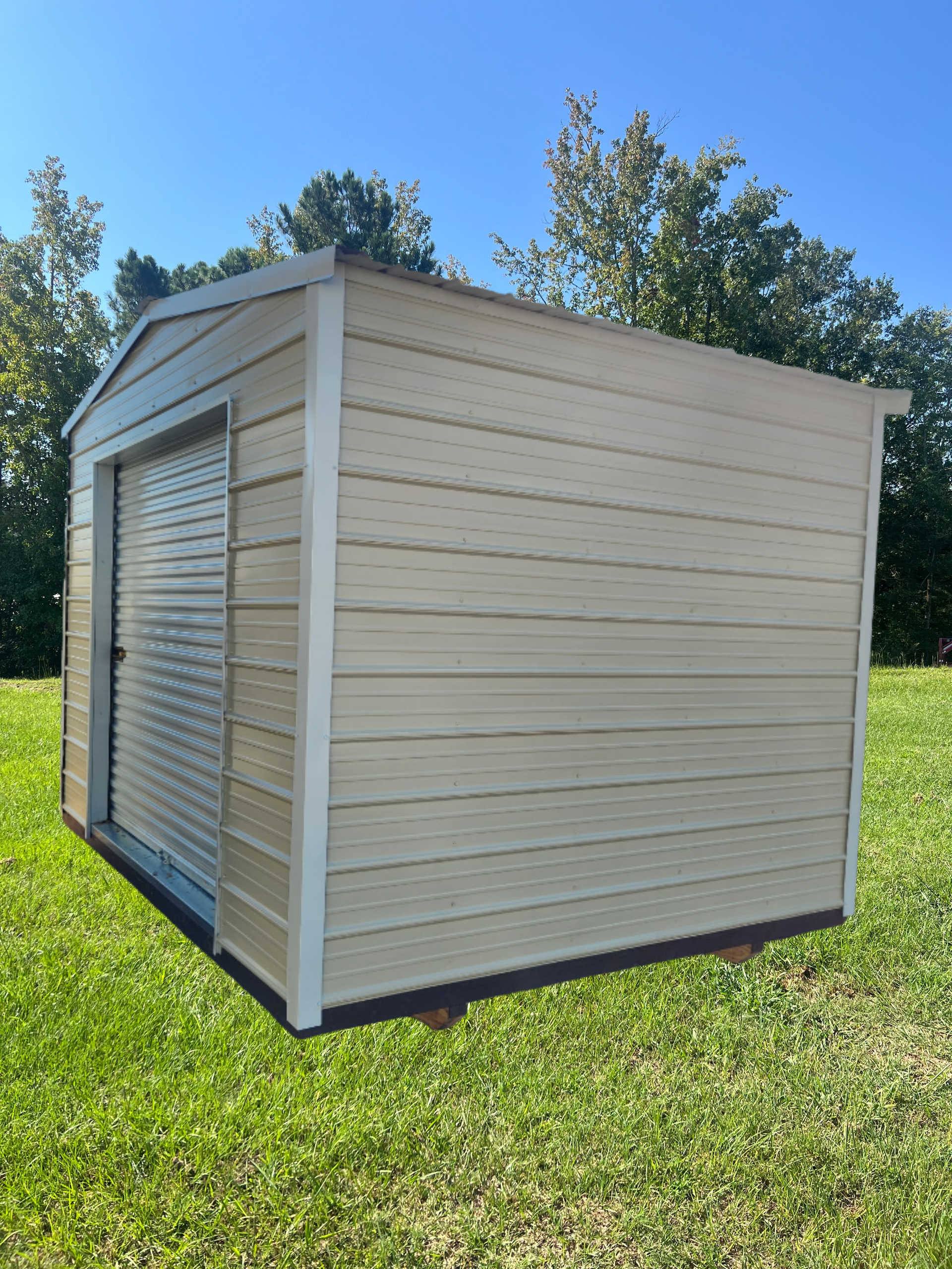 Small beige metal storage shed with a roll-up door on a grassy lawn under a blue sky