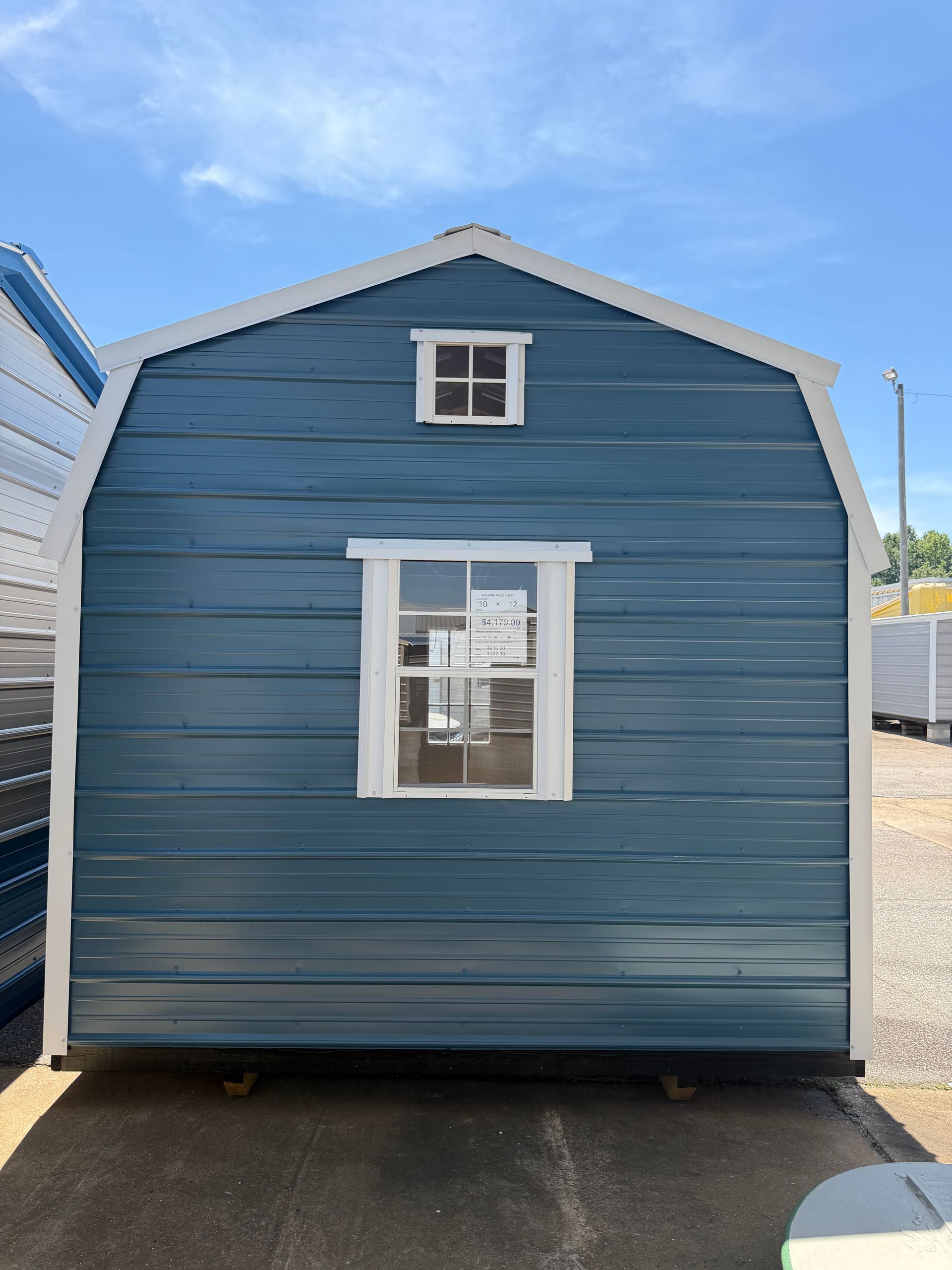 Blue shed with white trim and a small window, centered outdoors under a clear sky