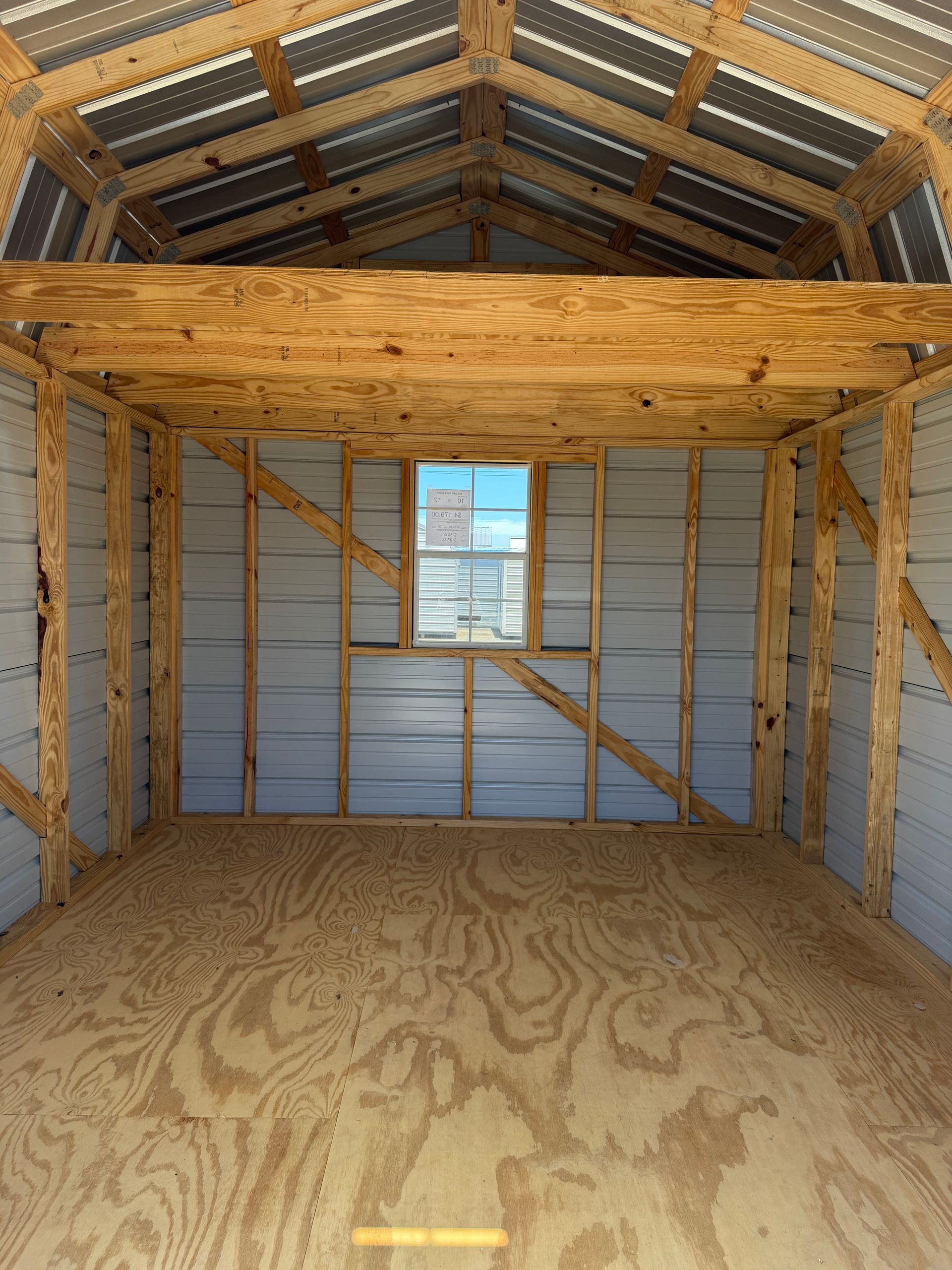 Inside a wooden shed, a plywood loft spans the back wall under a corrugated metal roof.