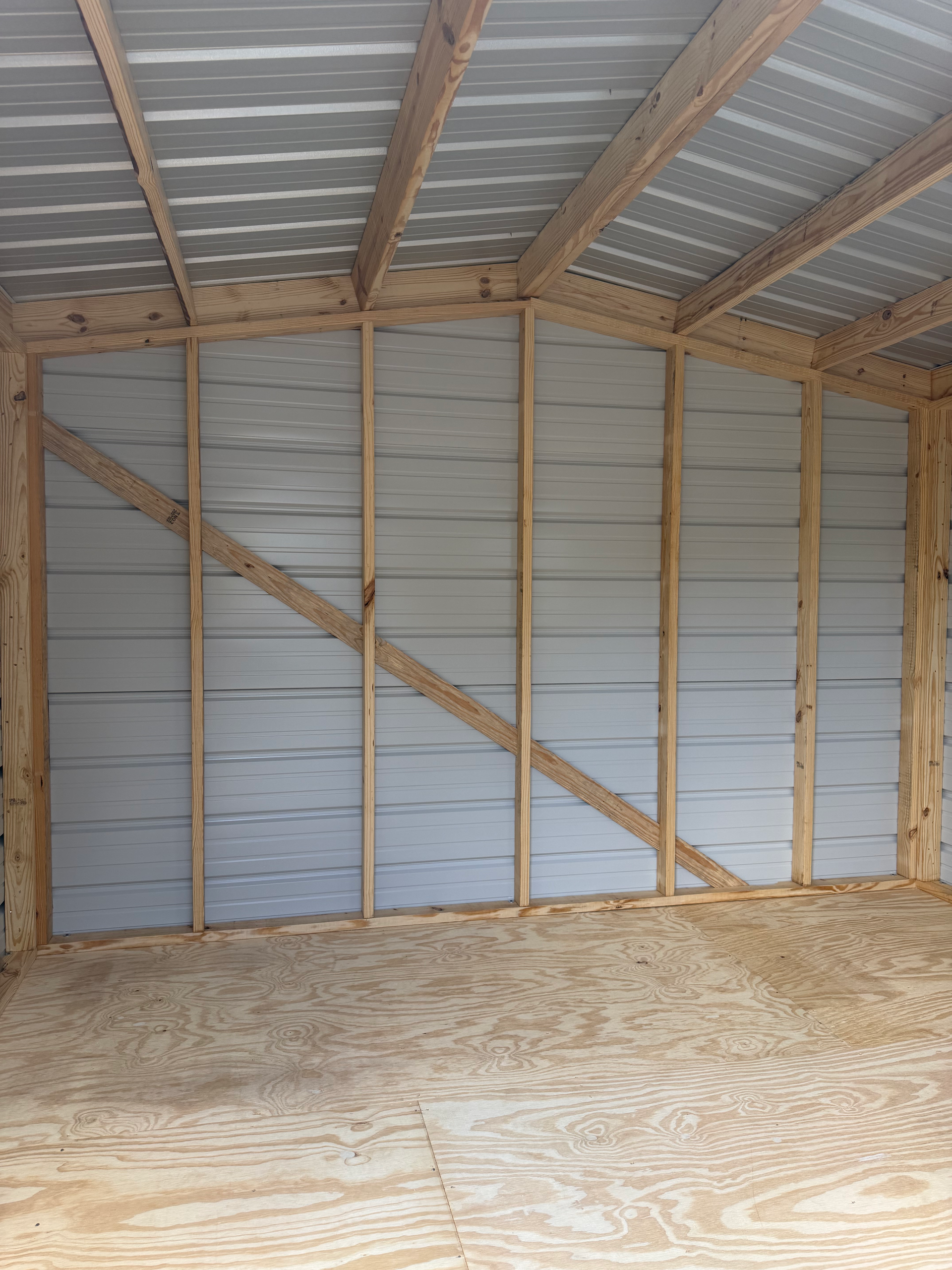 Empty wooden shed interior with corrugated metal walls, roof, and plywood floor