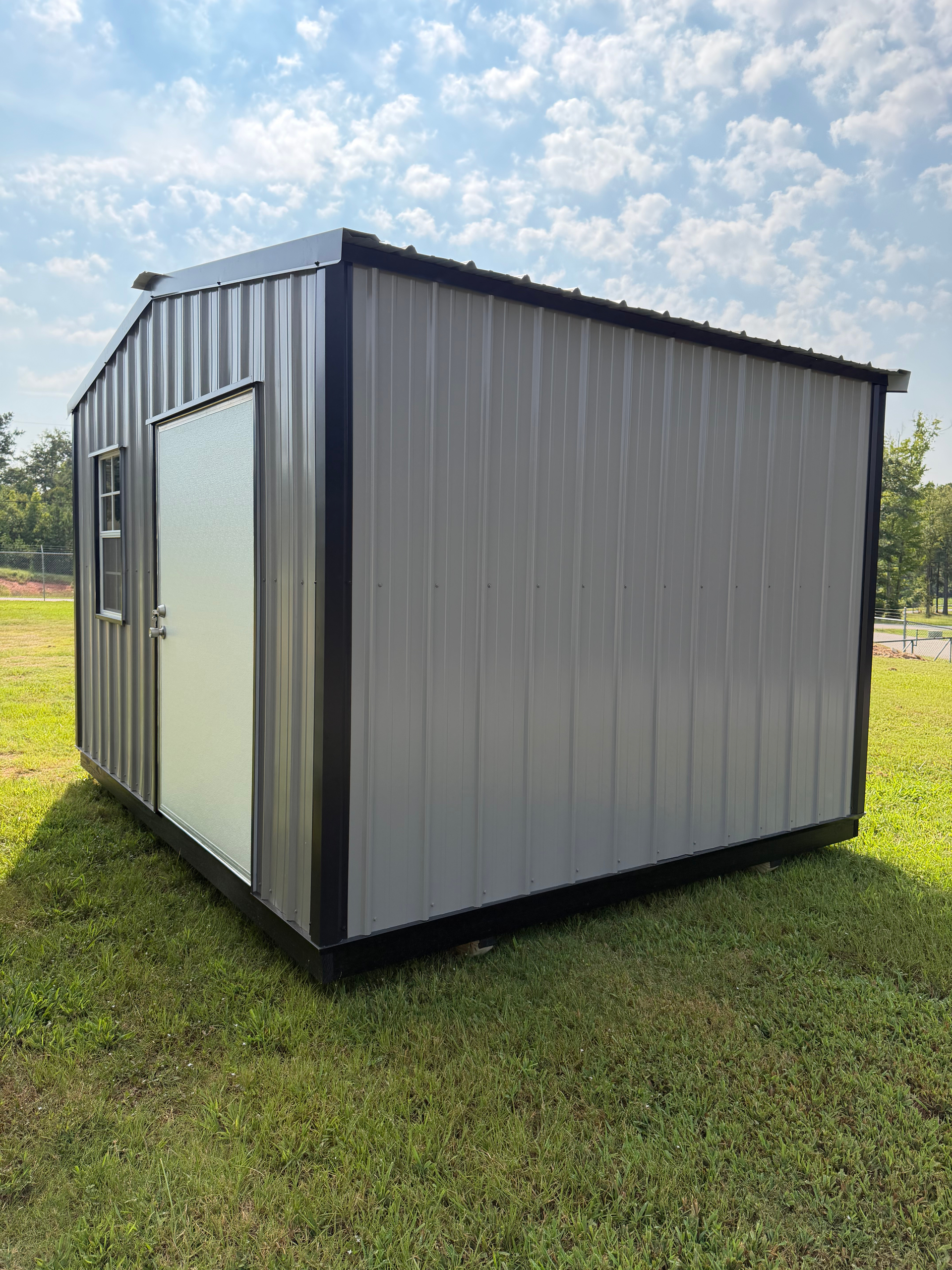 Small gray metal storage shed on grass under a partly cloudy sky.