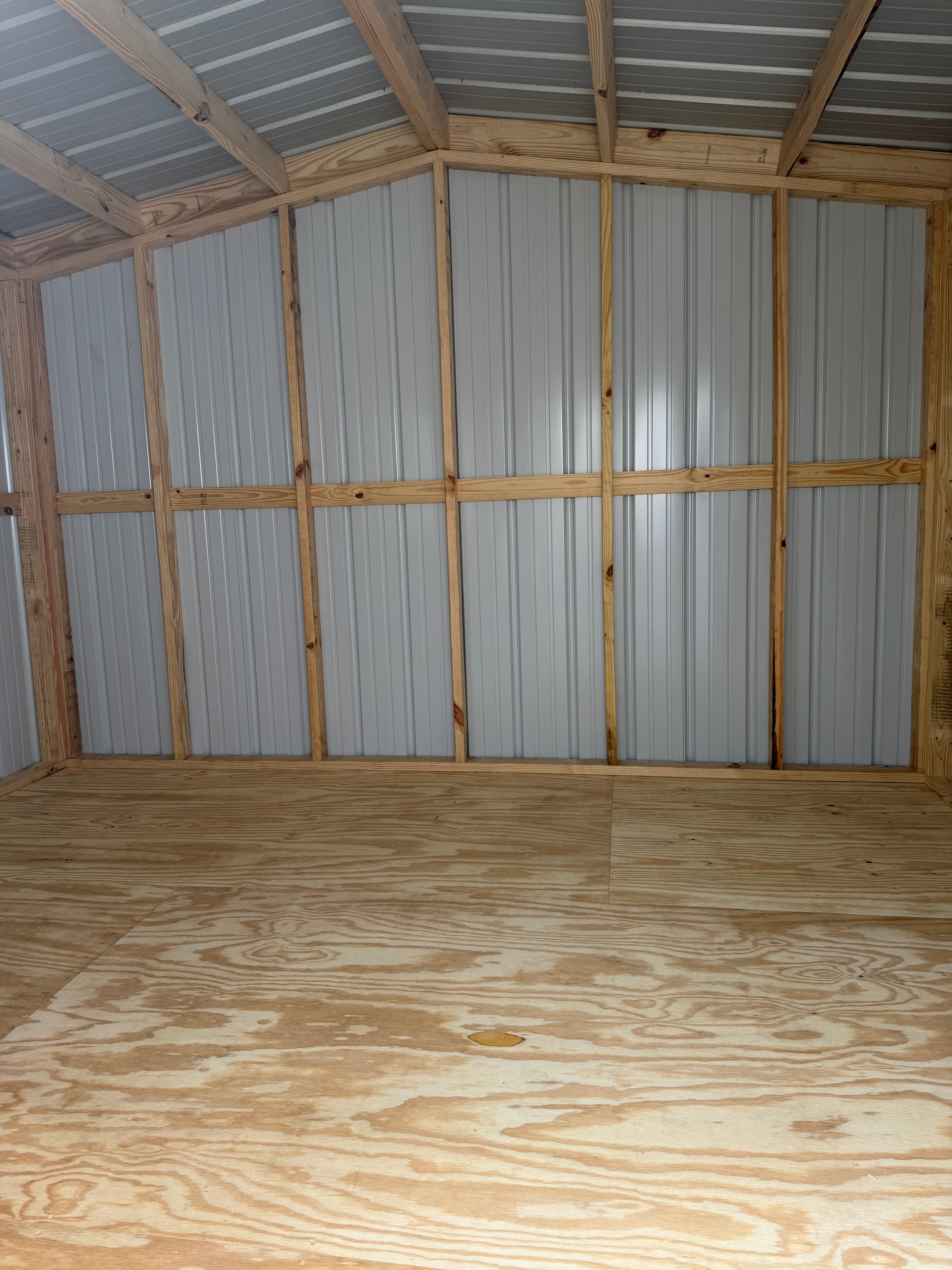 Empty unfinished shed interior with corrugated metal walls, exposed wood framing, and plywood floor