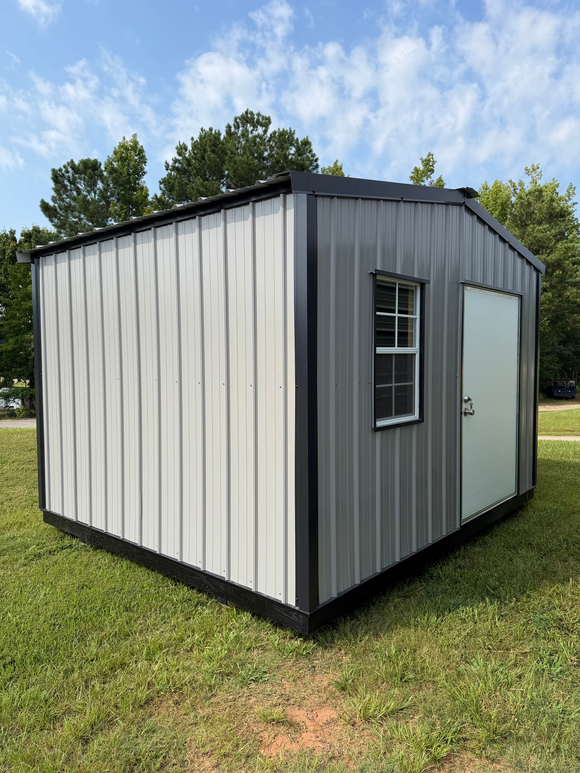 Small gray metal shed with a window and door sitting on grass under a blue sky