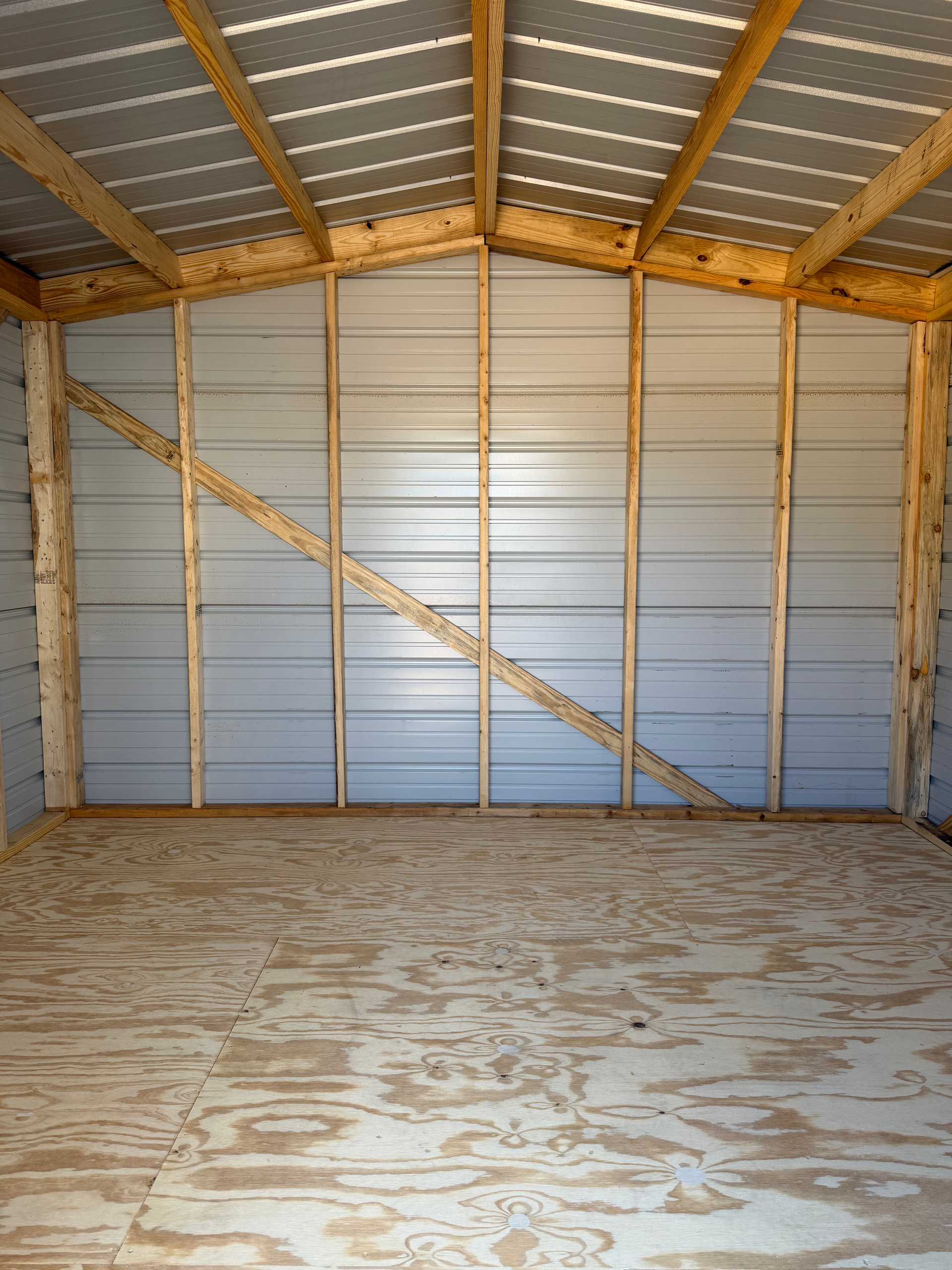 Empty metal shed interior with exposed wooden framing and plywood floor.