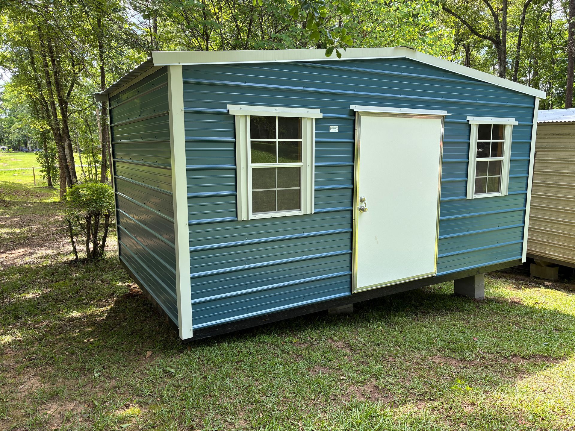 Small blue shed with white trim and door in a grassy wooded area
