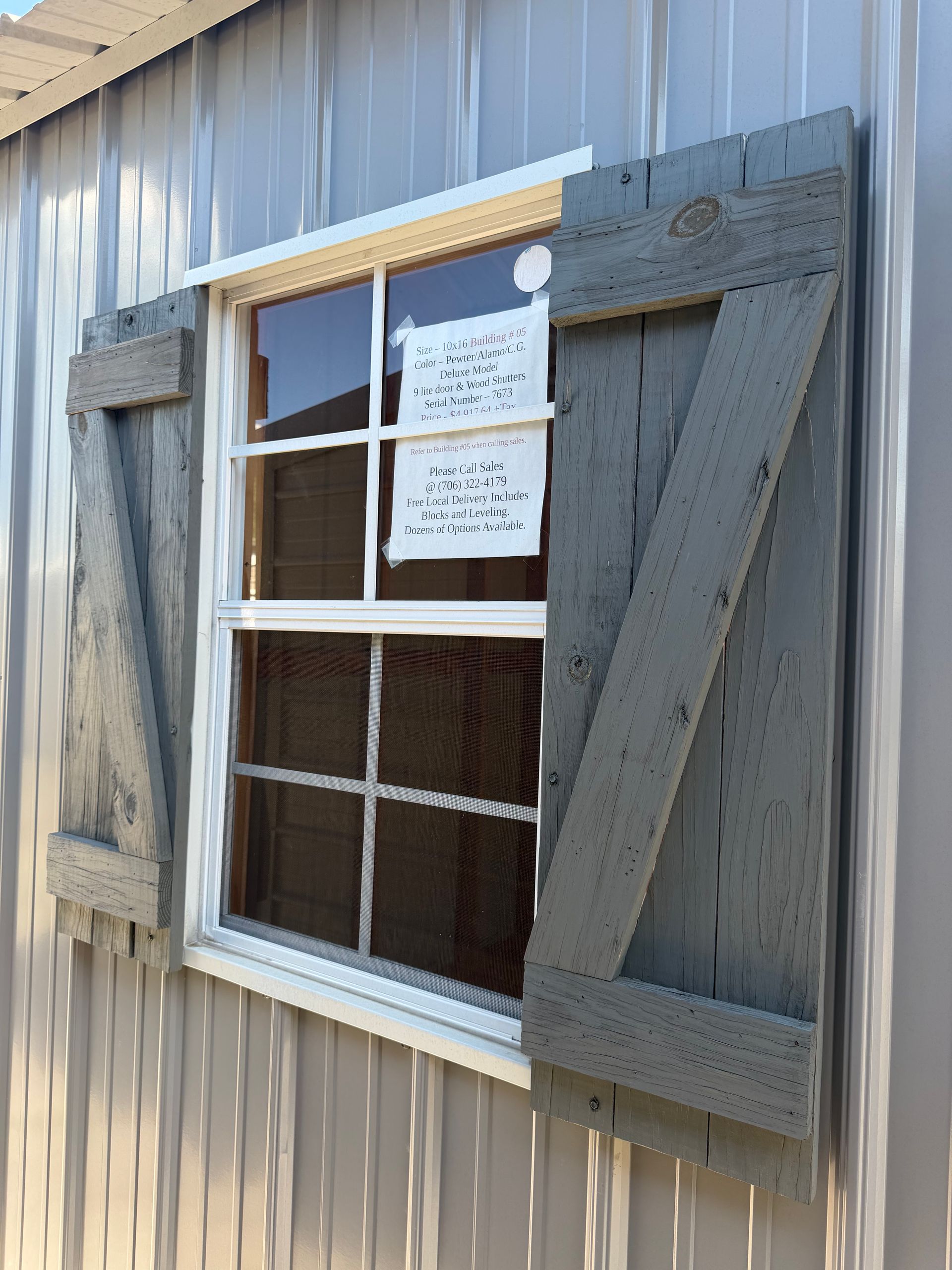 Weathered gray shutters framing a white-trimmed window on a corrugated metal wall.