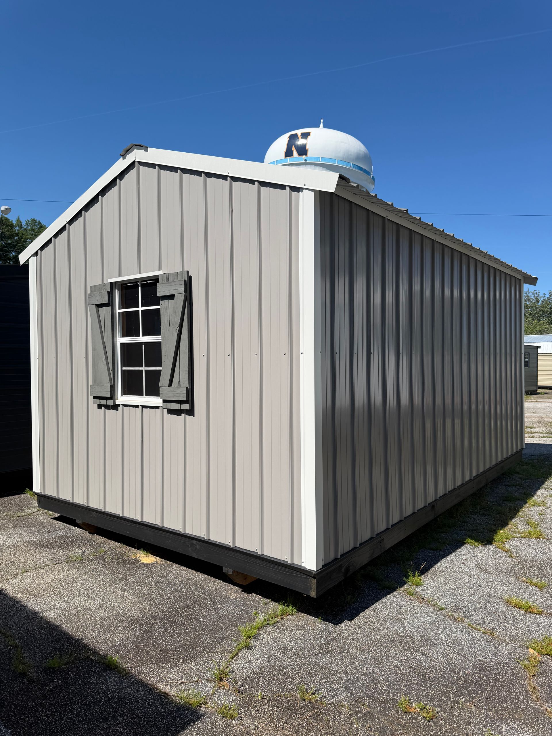 Small beige shed with a window and dome vent, standing on gravel under a clear blue sky