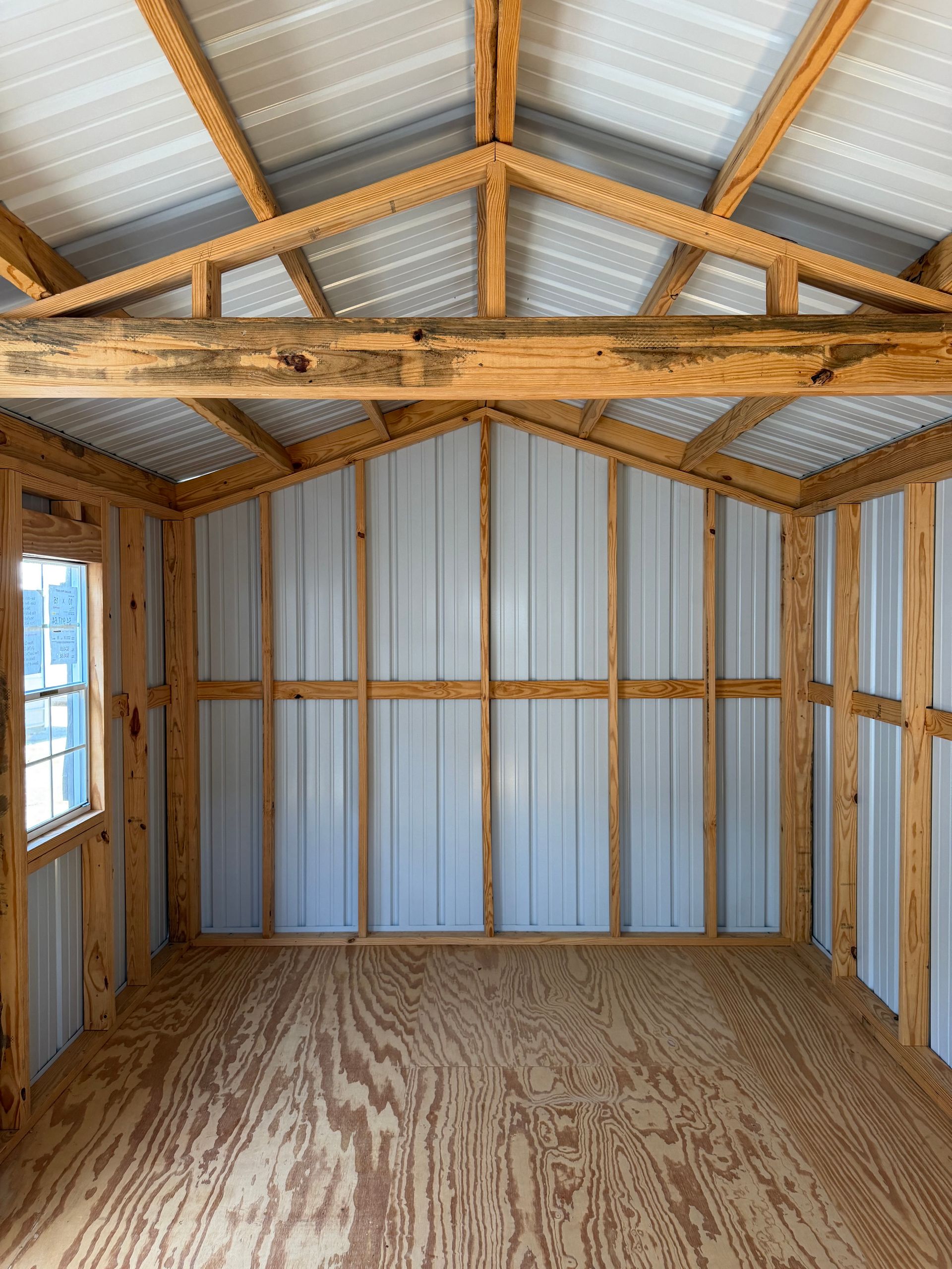 Empty wooden shed interior with corrugated metal walls, exposed rafters, and plywood floor.