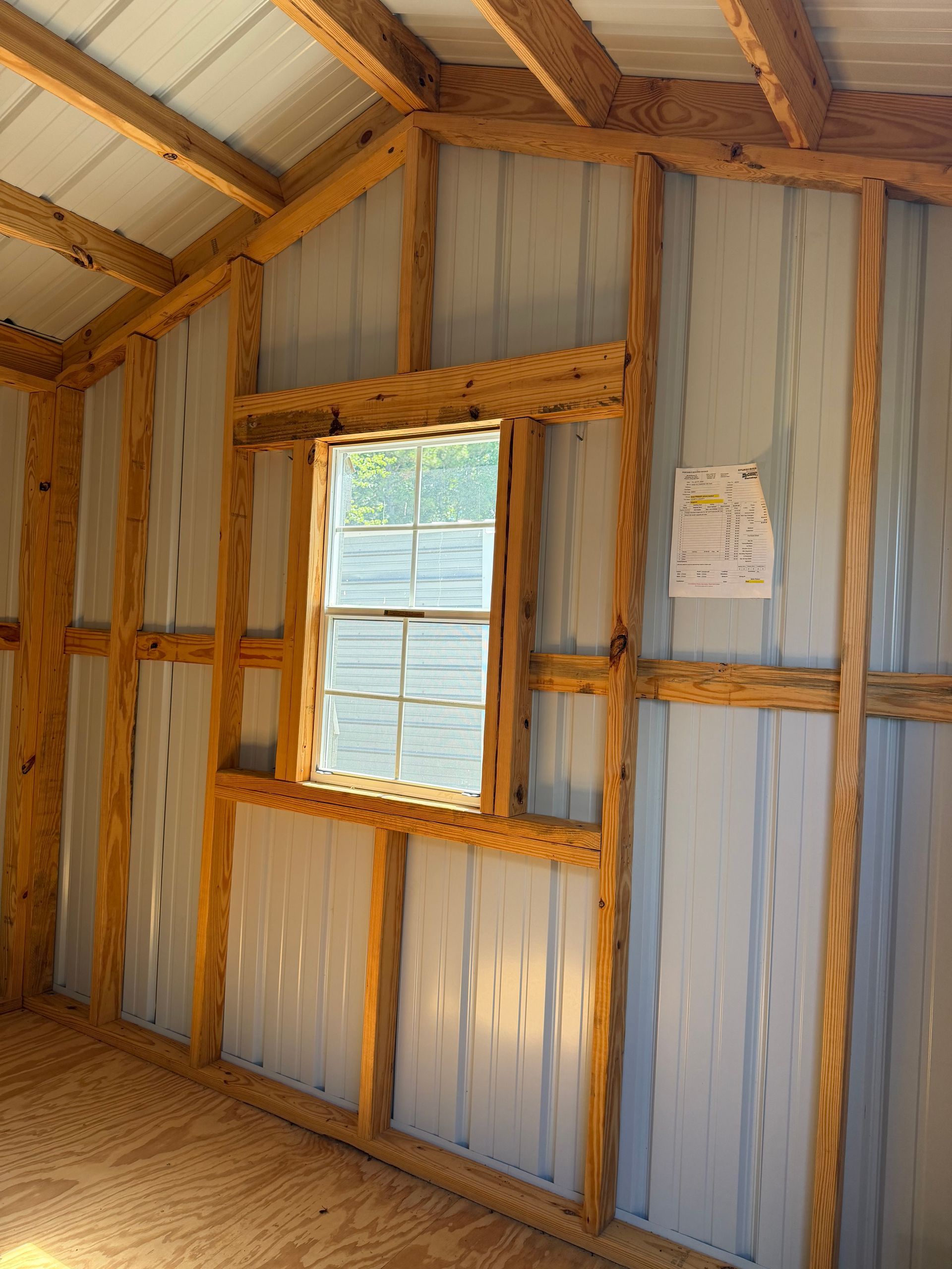 Wood-framed shed interior with corrugated metal walls, a window, and a wooden floor.