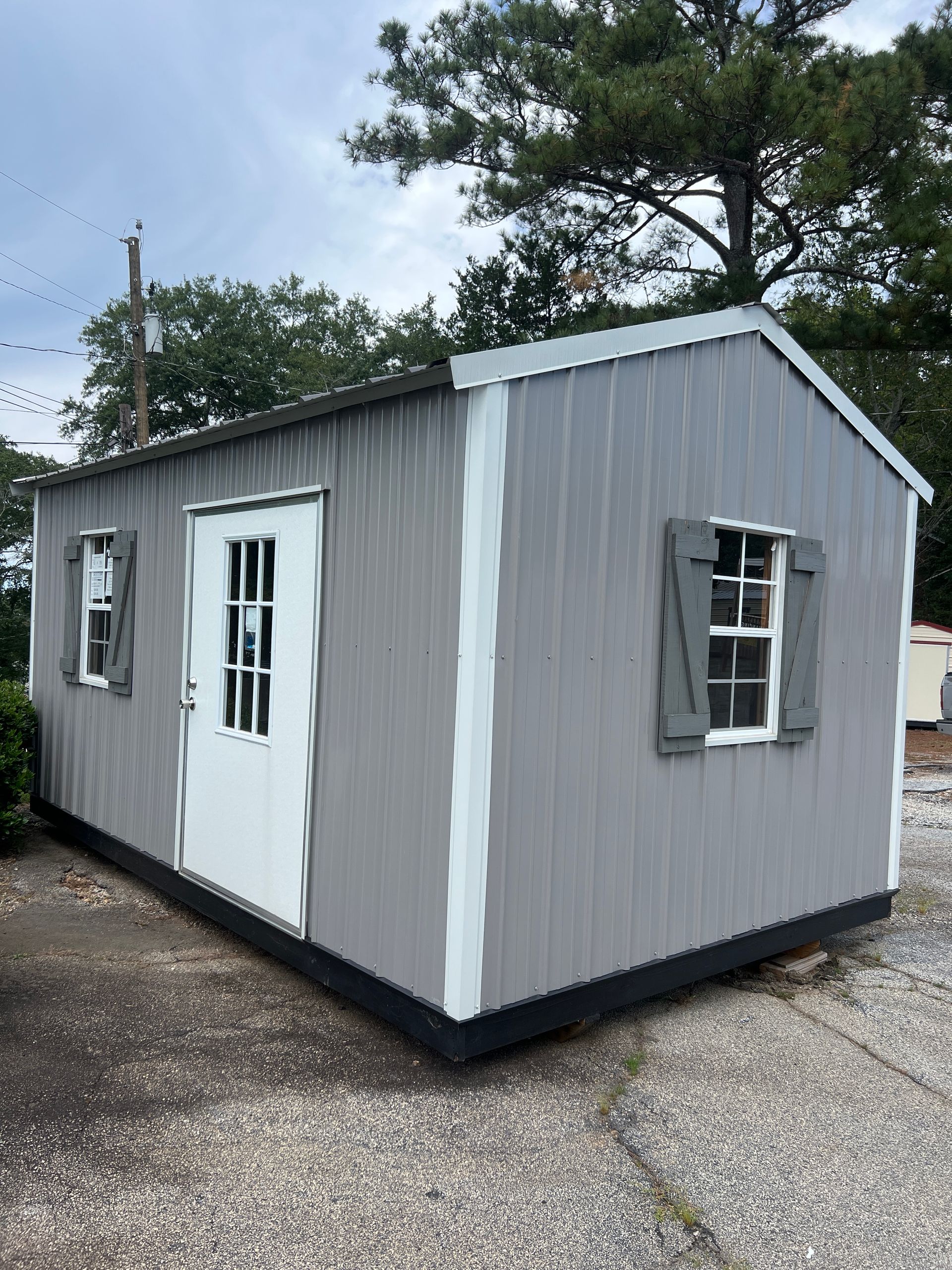 Small beige shed with white-trim windows and a blue water tower in the background, on a gravel lot.