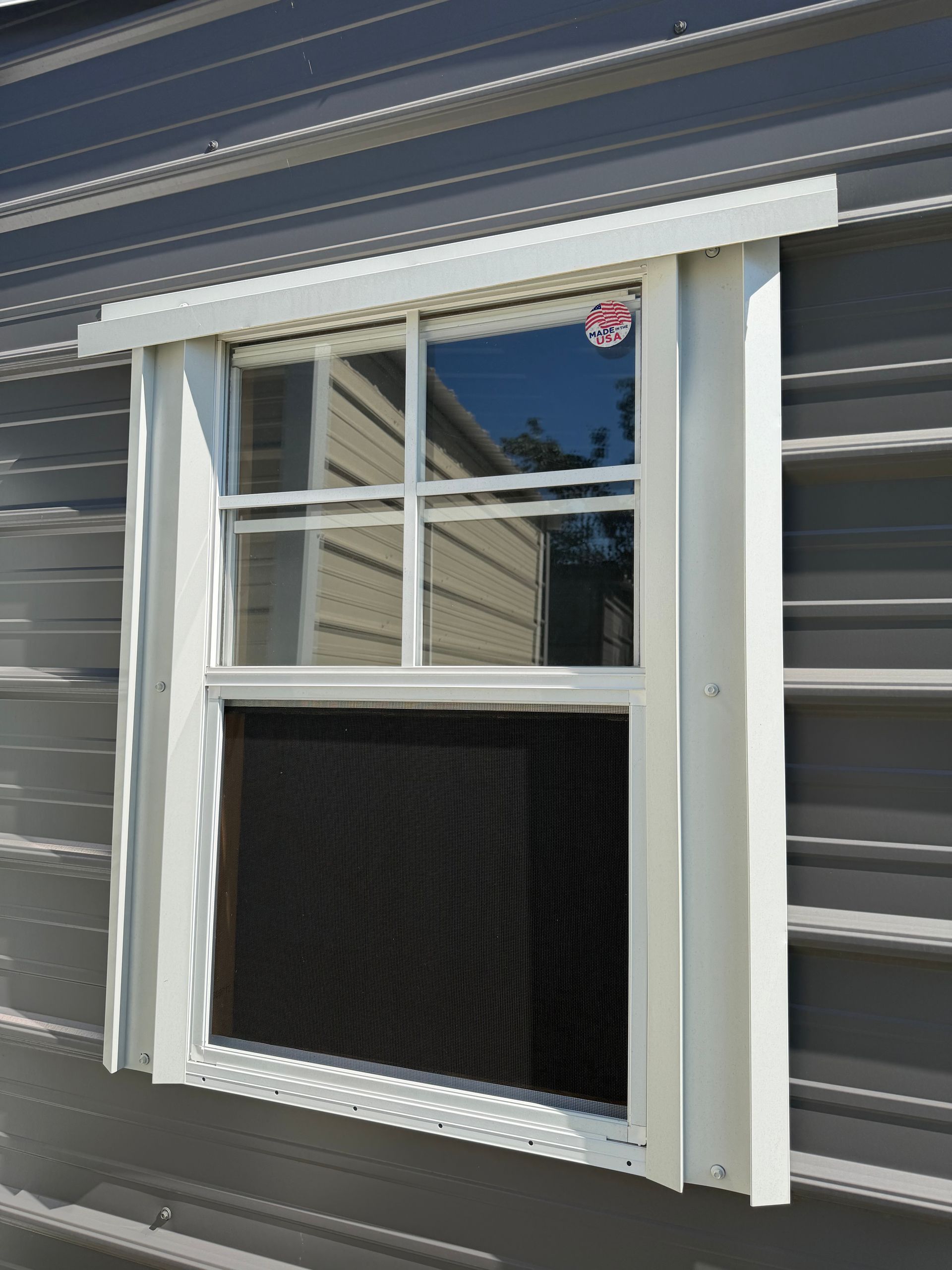 White-trimmed window air conditioner in a gray-sided house, with a second-screen panel below the open sash.