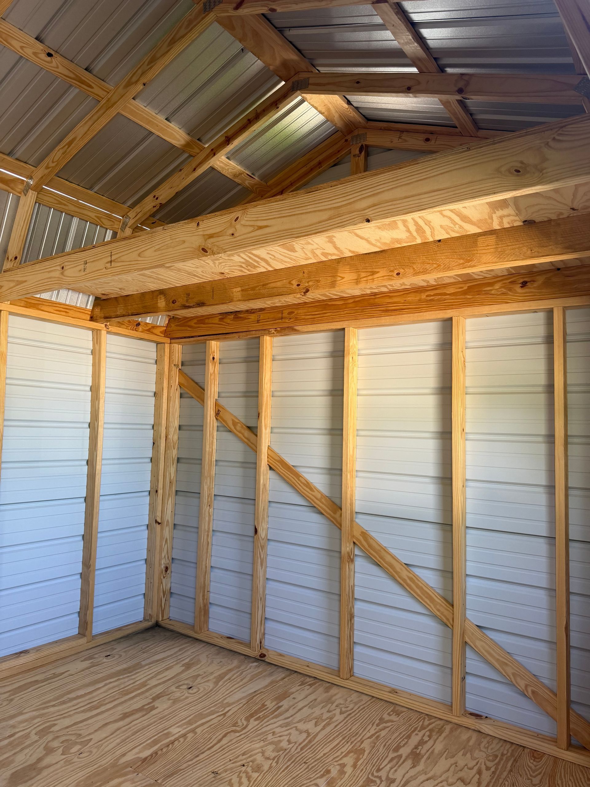 Interior of an unfinished wooden shed with exposed beams, corrugated metal roof, and plywood floor.
