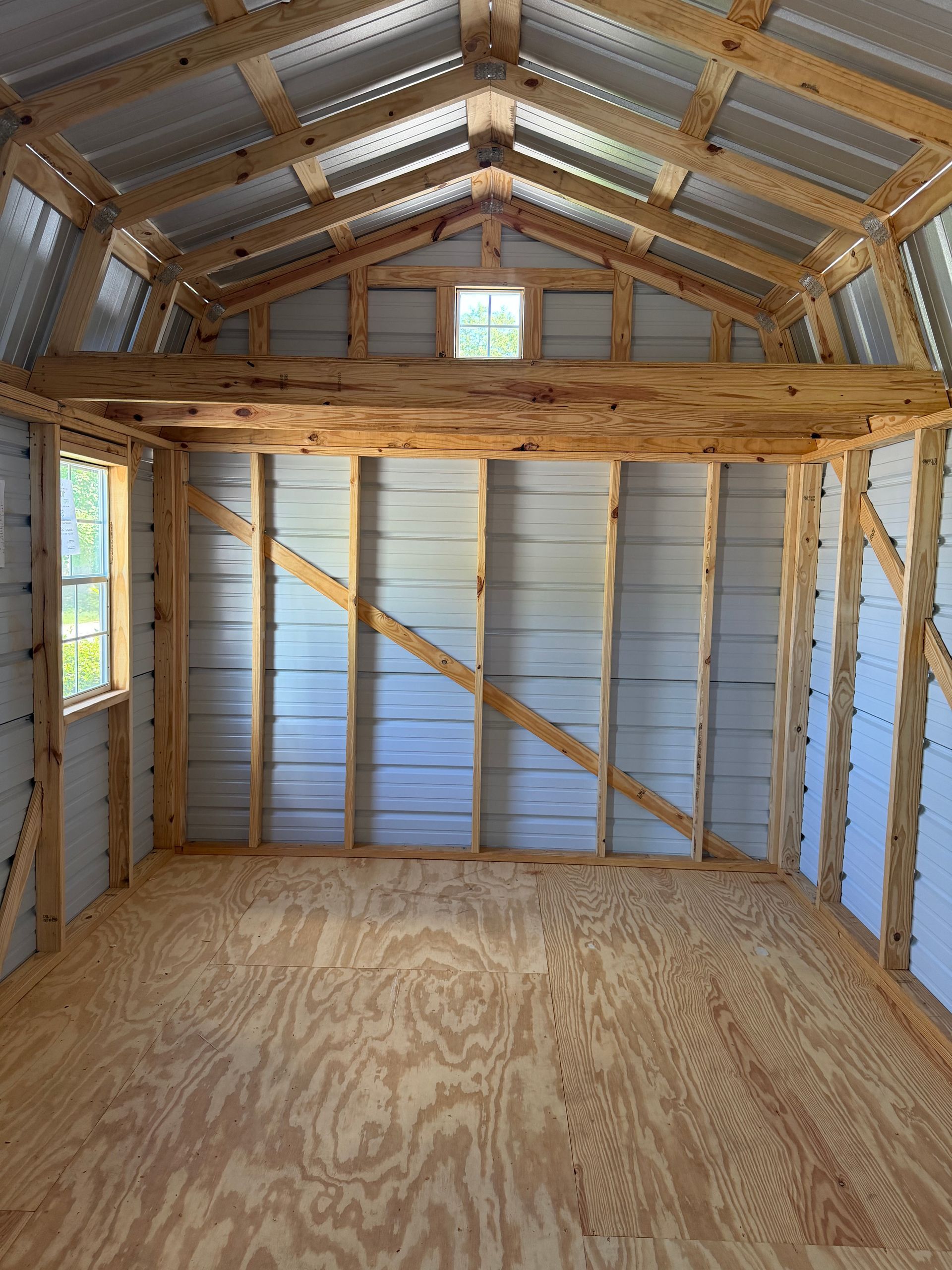 Empty small shed interior with plywood floor, exposed wood framing, corrugated metal walls, and a loft platform.