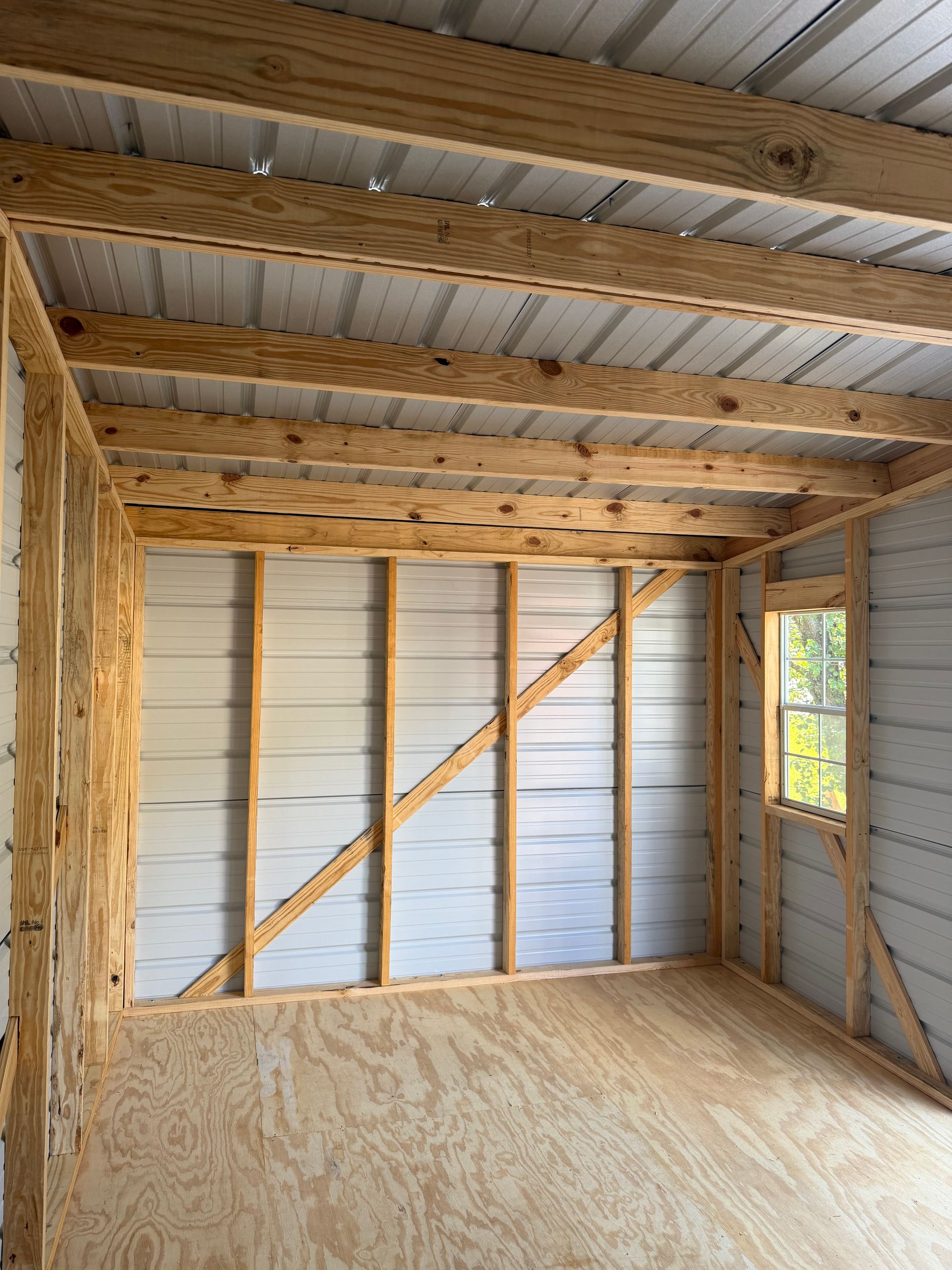 Empty unfinished room with exposed wood framing, white walls, and plywood floor under construction