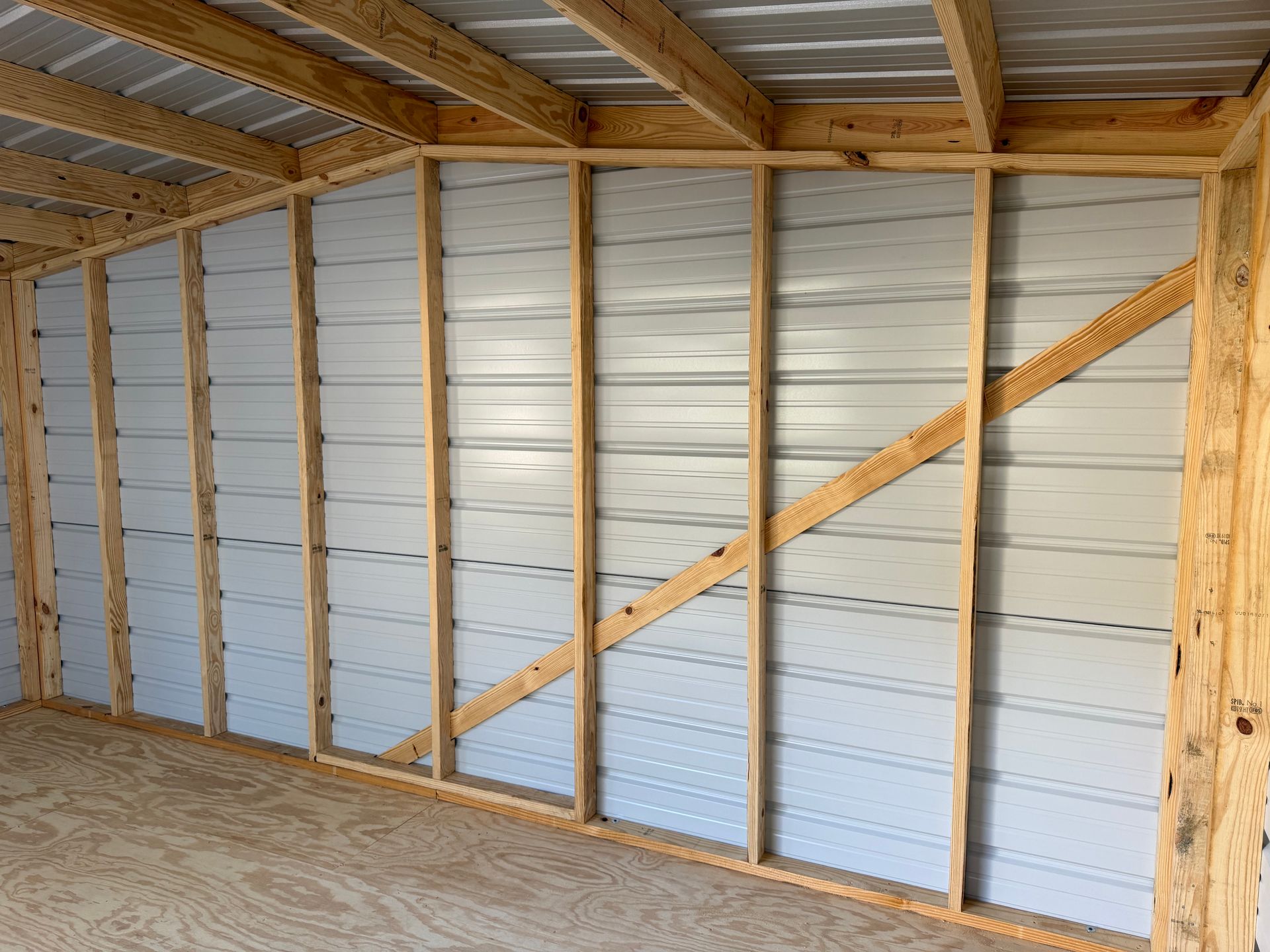 Empty metal-walled shed interior with exposed wooden framing and plywood floor