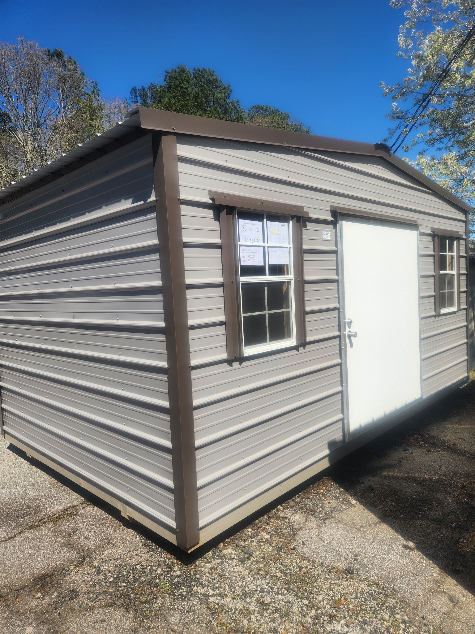 Small beige shed with white door and window under a blue sky outside.