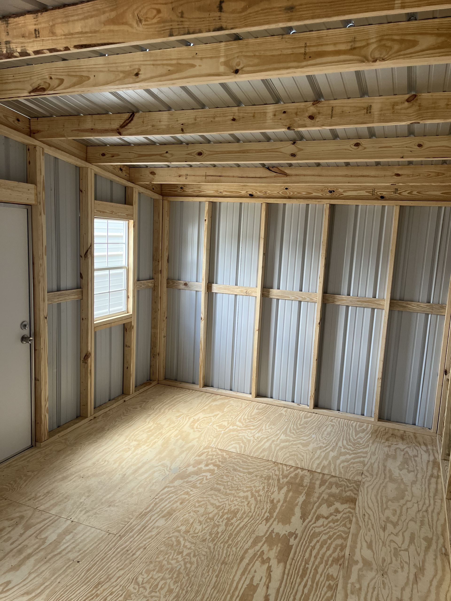 Unfinished room with exposed wooden studs, OSB floor, and insulated wall paneling around a small window.