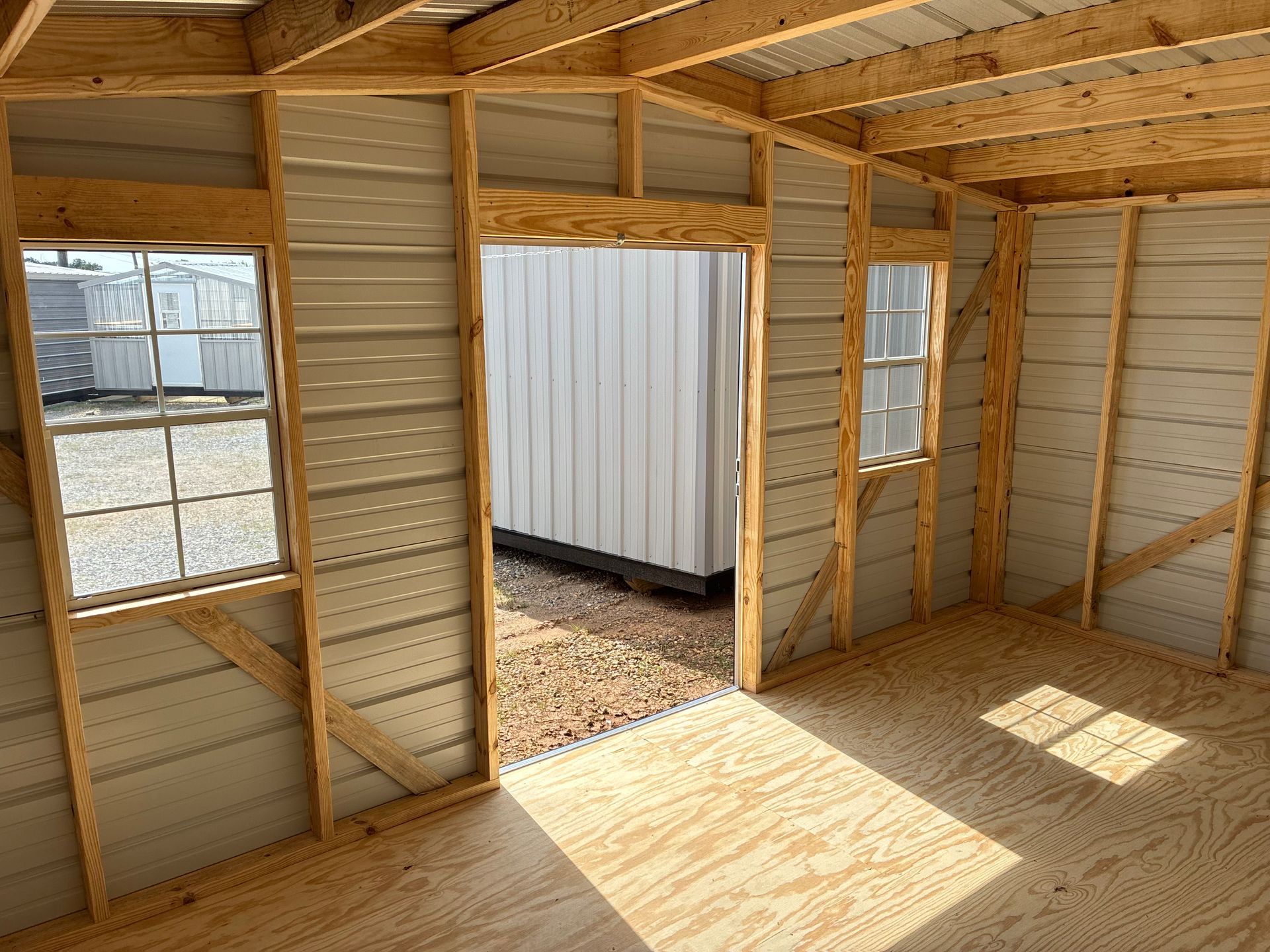 Inside a small unfinished shed, sunlight streams through the doorway and windows onto bare wooden walls.