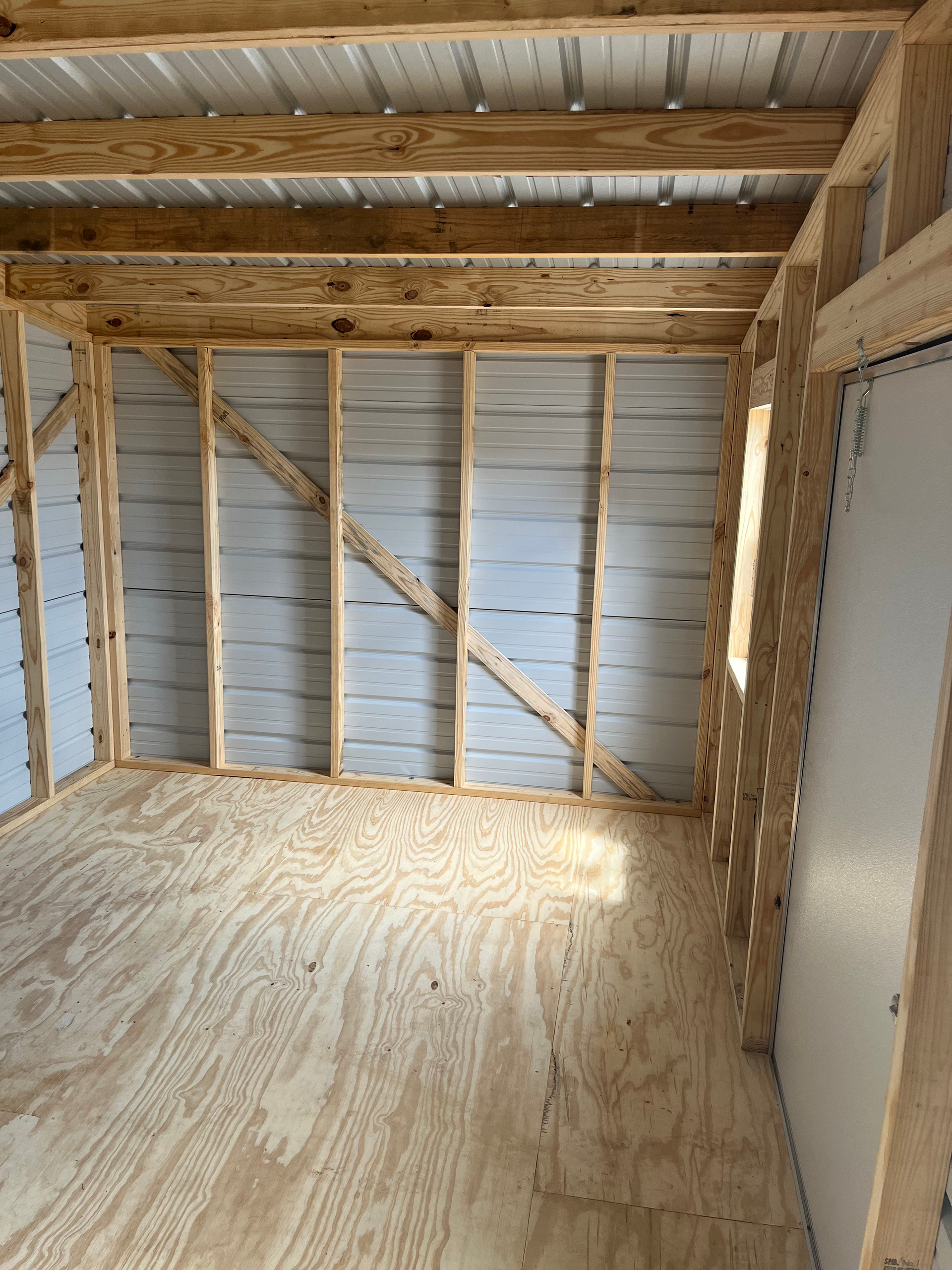 Empty unfinished wooden room with exposed framing, plywood floor, and metal roof panels