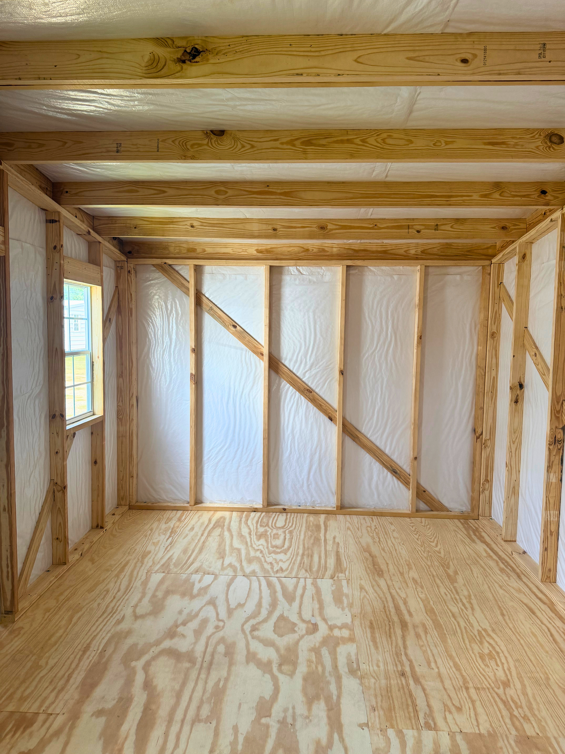Inside a small unfinished wooden shed with plywood walls, floor, and exposed ceiling beams.
