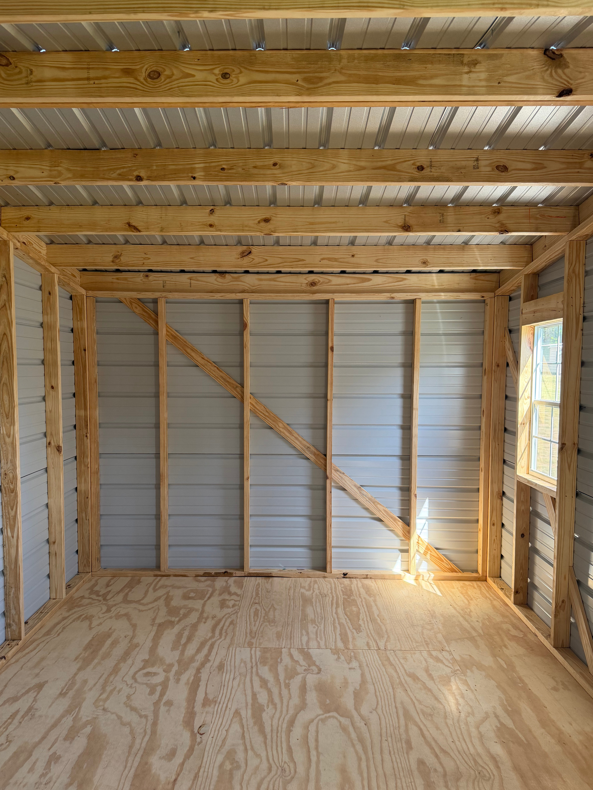 Empty wooden shed interior with exposed framing, plywood floor, and a sunlit wall opening