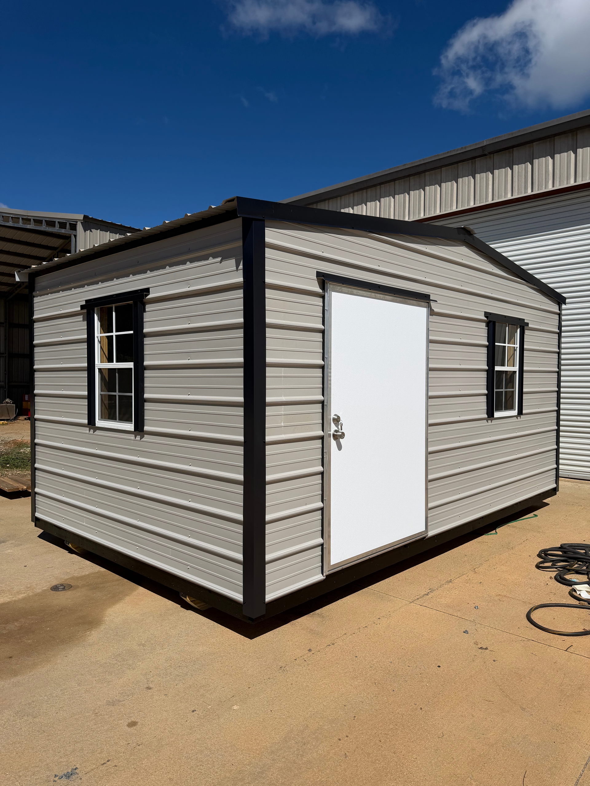 Small gray shed with black trim and white door on a sunny outdoor lot.