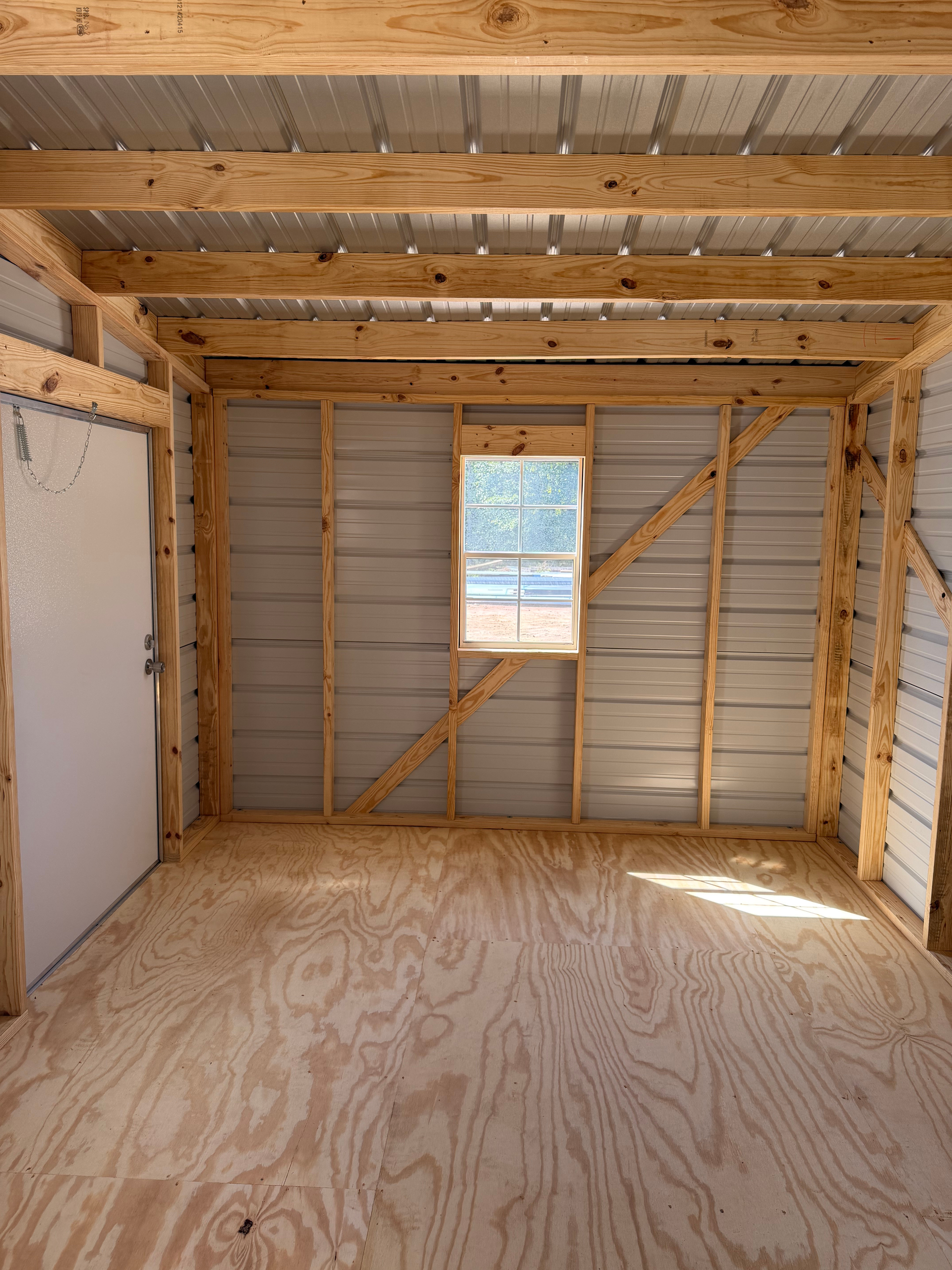 Partially finished room with plywood floor, exposed studs and rafters, and a small window on the far wall