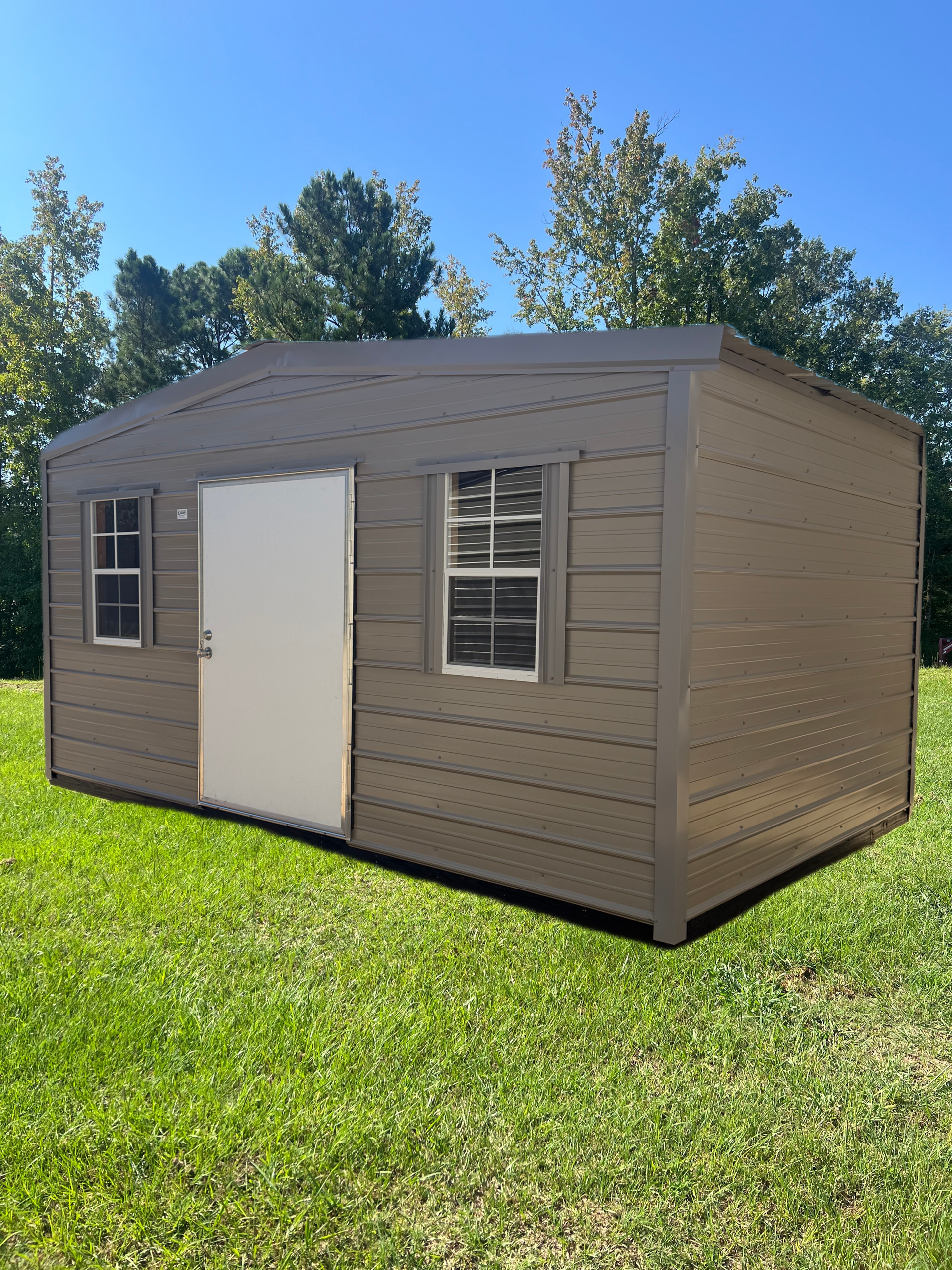 Tan shed with white door and windows on a grassy lawn under a blue sky