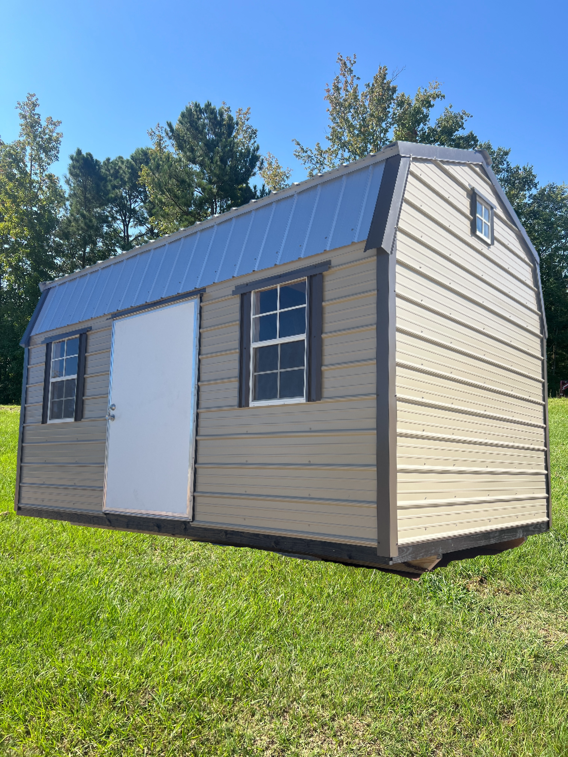 Small tan shed with blue roof and white door on grassy lawn under a clear sky