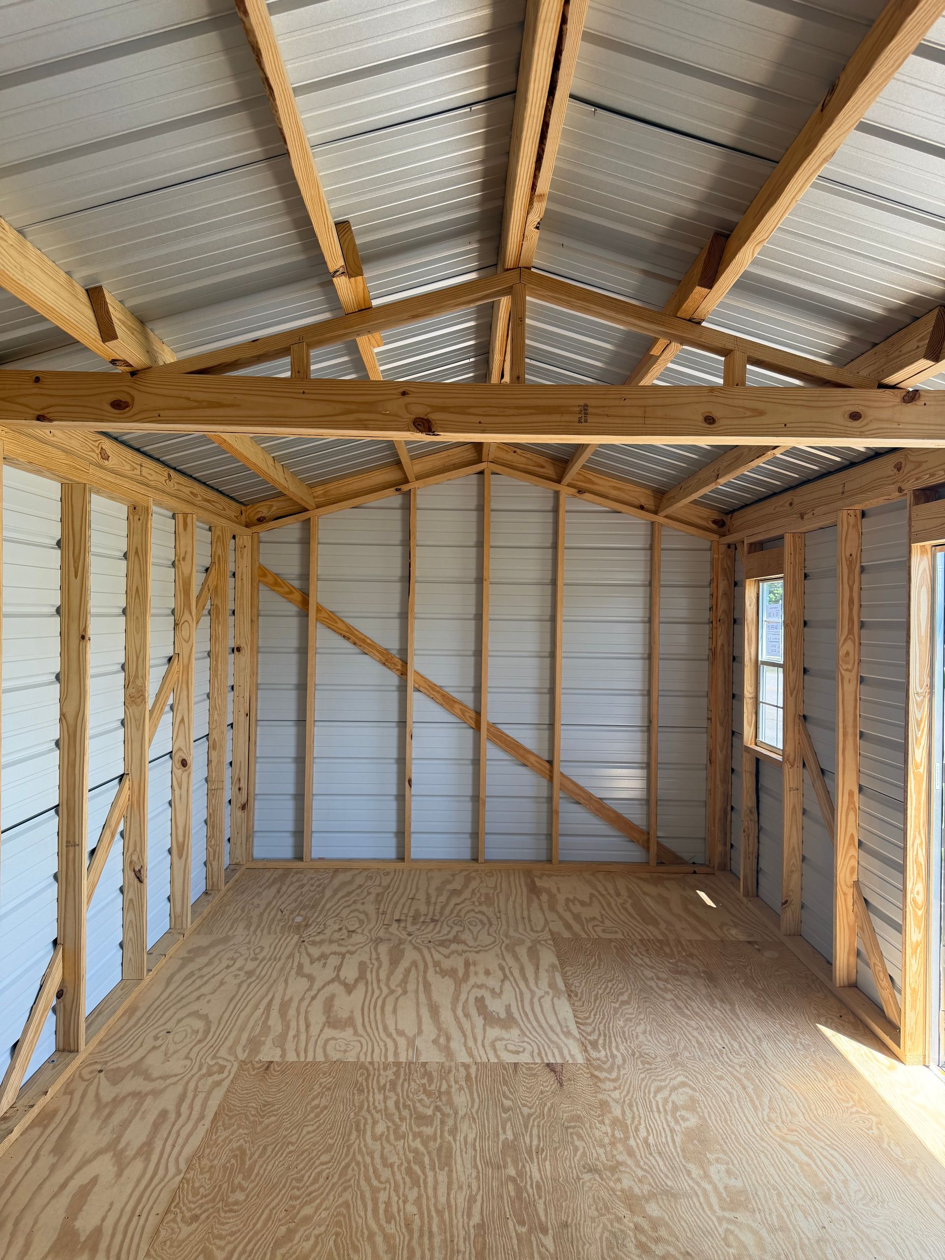 Empty unfinished wooden shed interior with plywood floor, exposed studs, and metal roof panels