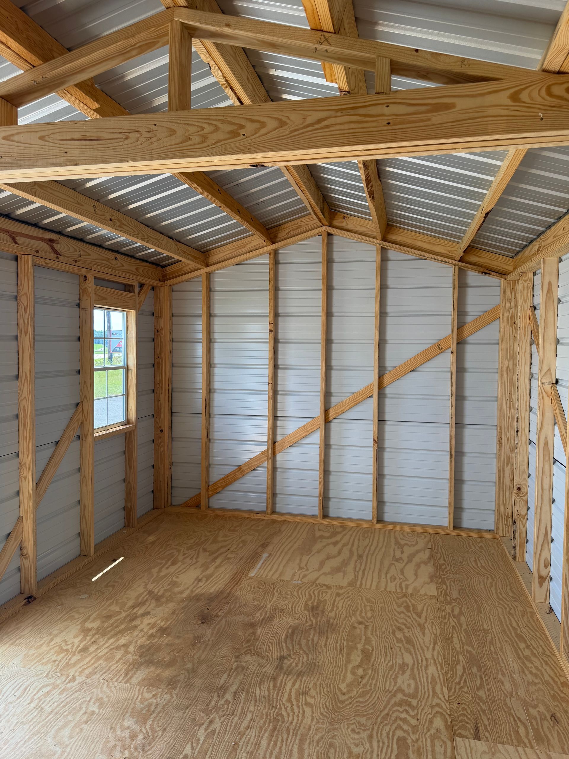 Empty wooden shed interior with exposed rafters, metal walls, and plywood floor