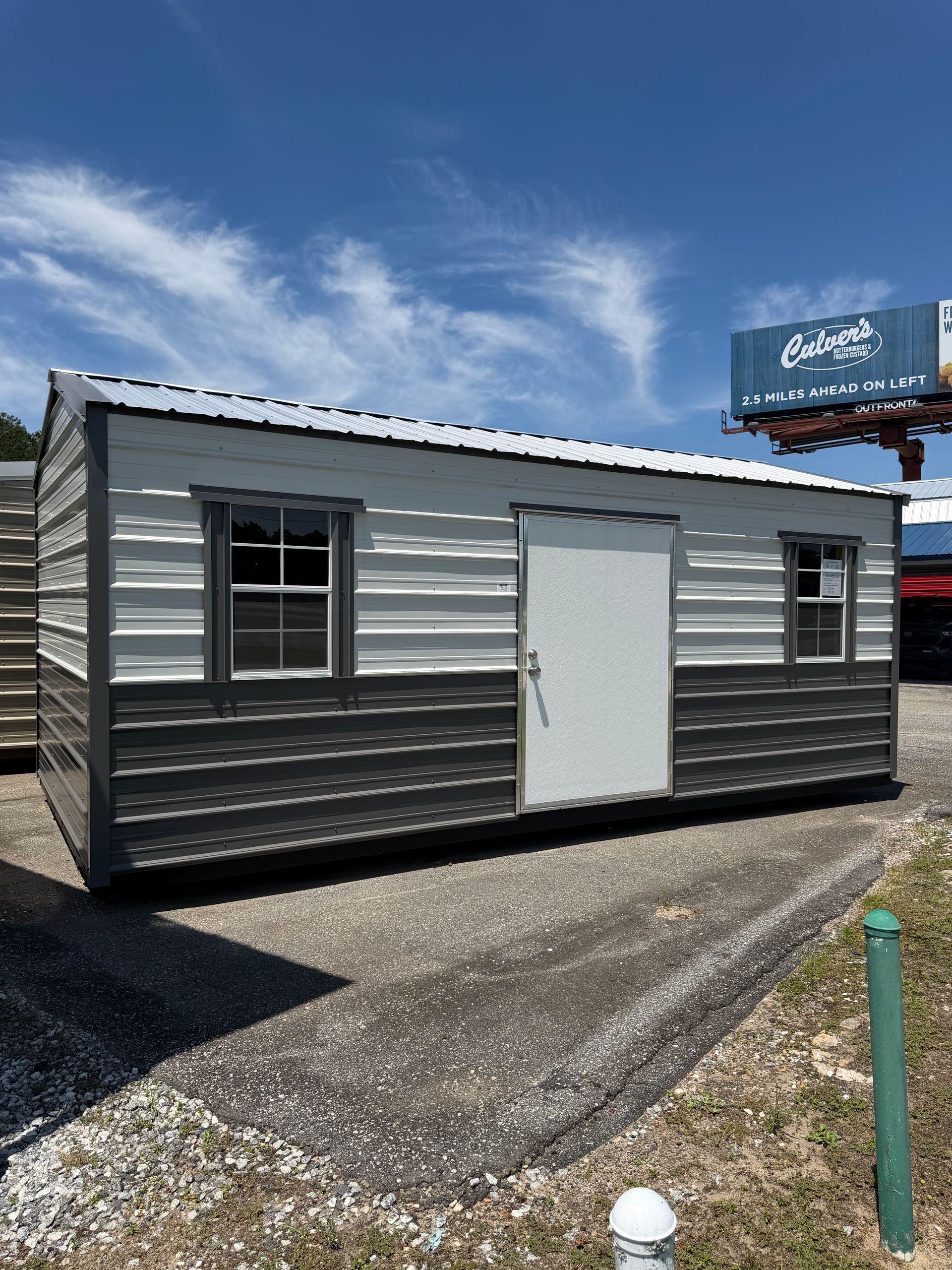 Small silver metal building with white door and windows on a gravel lot under a blue sky