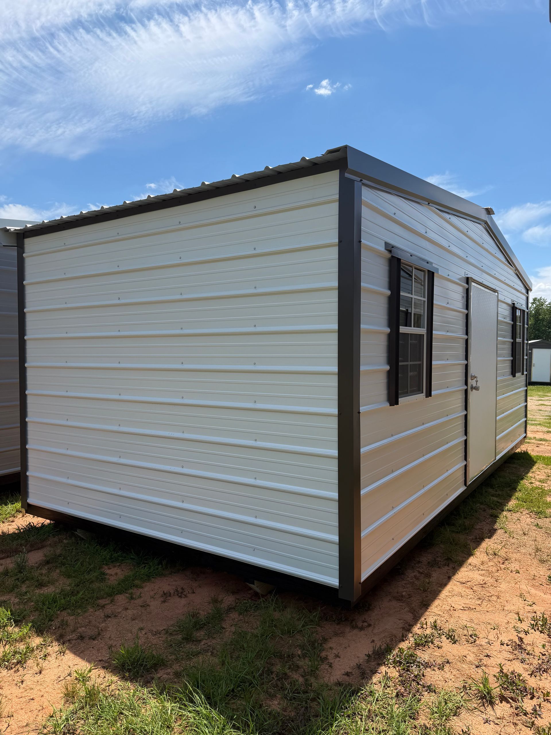 Small white portable building with black trim and a window, set on a dirt lot under a blue sky