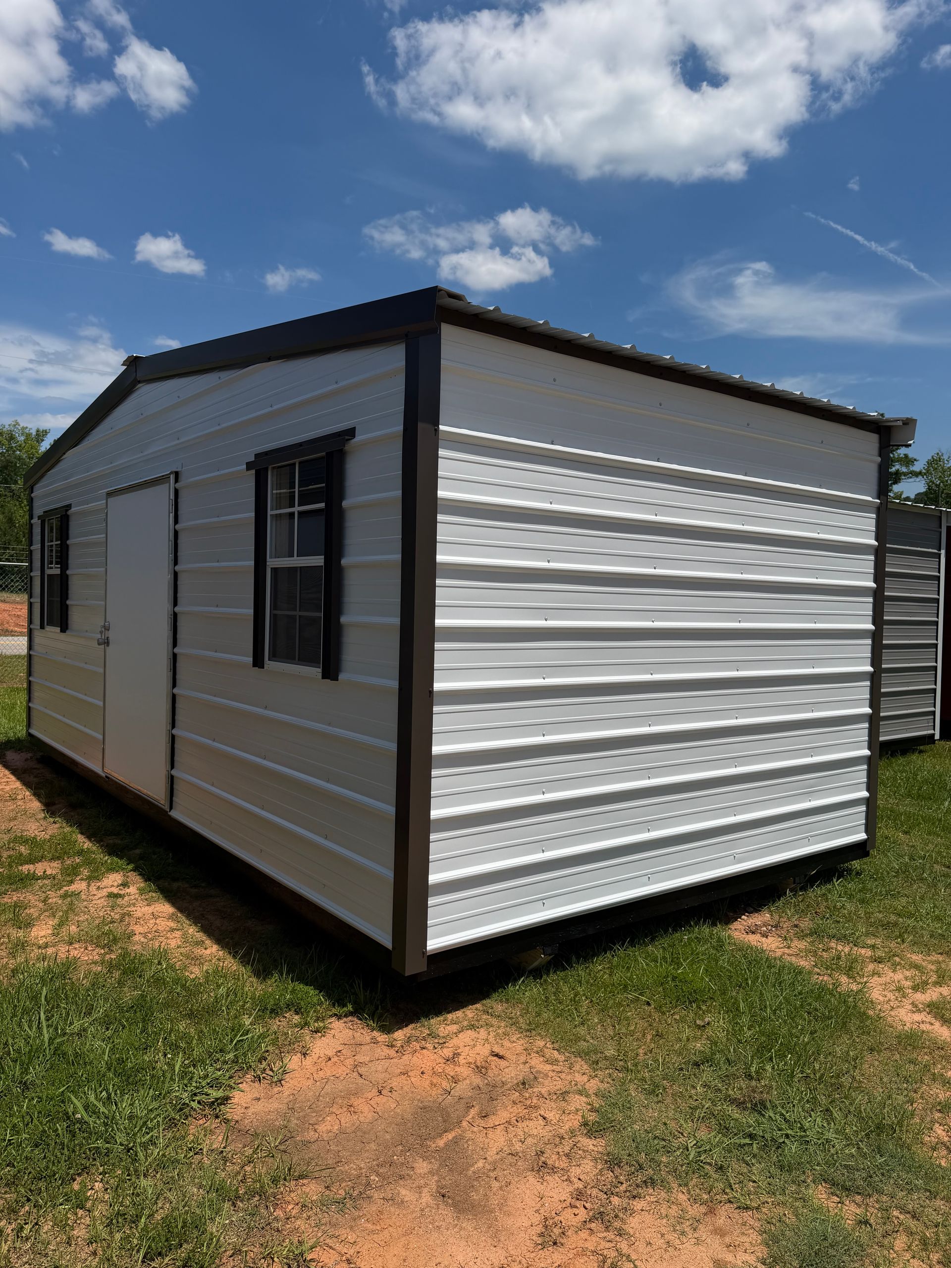 Small white portable building with black trim and windows on a grassy lot under a blue sky.