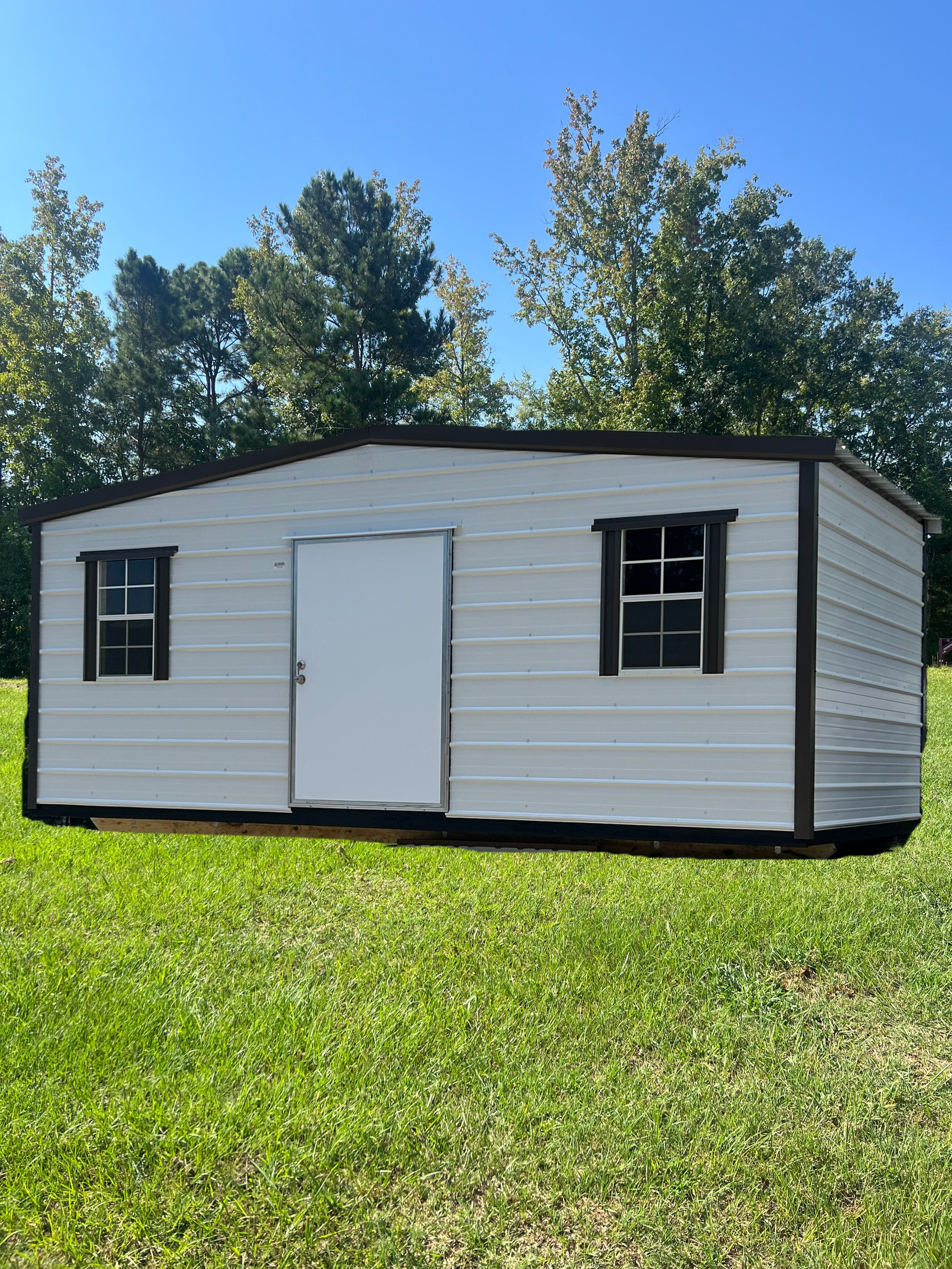 Small white shed with black trim and two windows on a grassy lawn under a blue sky.