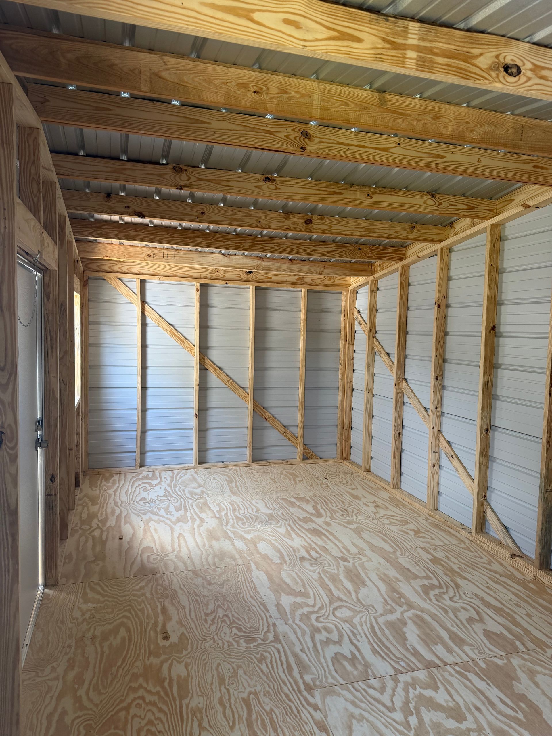 Unfinished room with exposed wooden beams, plywood floor, and white insulated walls with diagonal bracing.