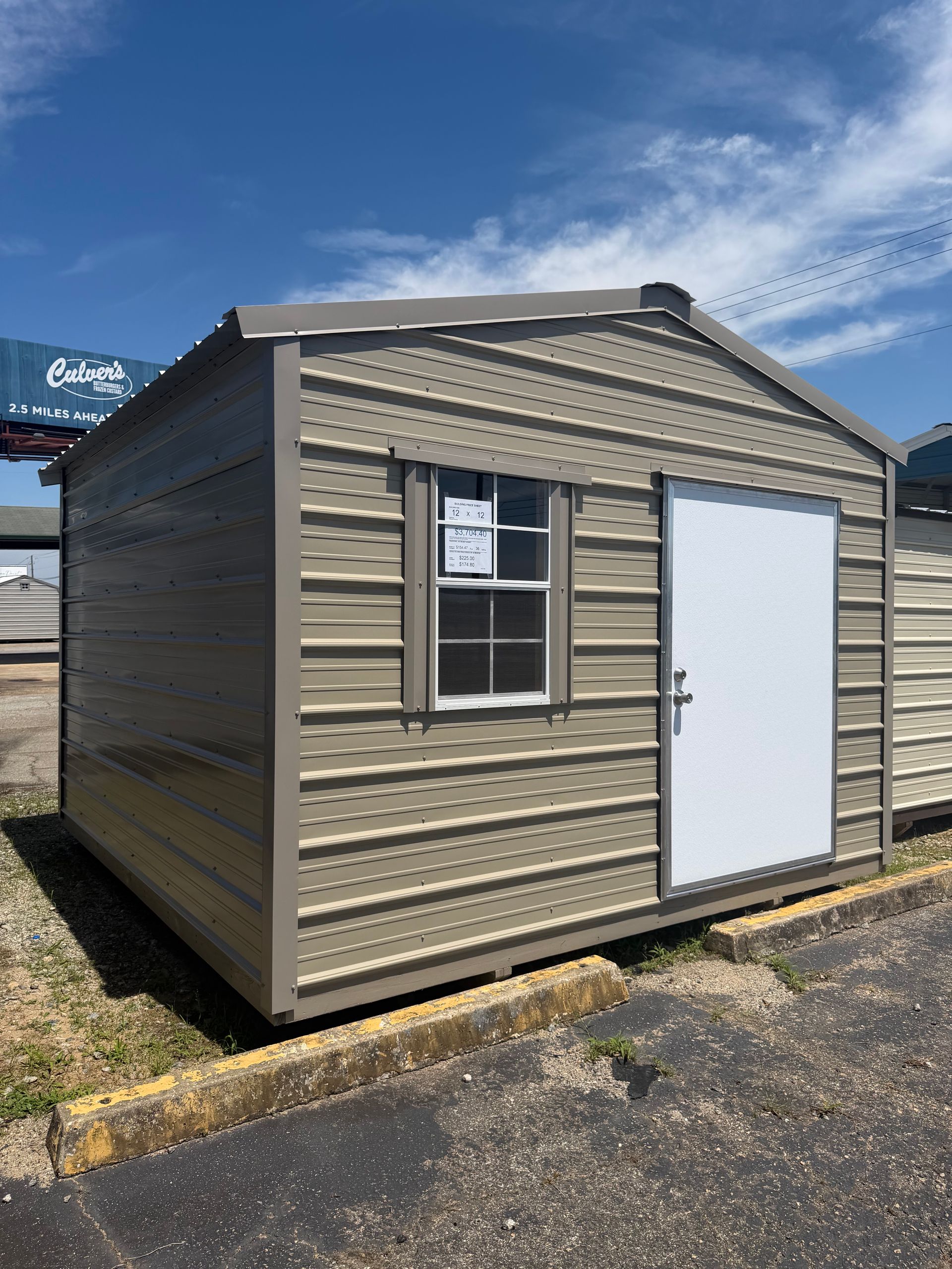Small beige shed with a window and white door on a gravel lot