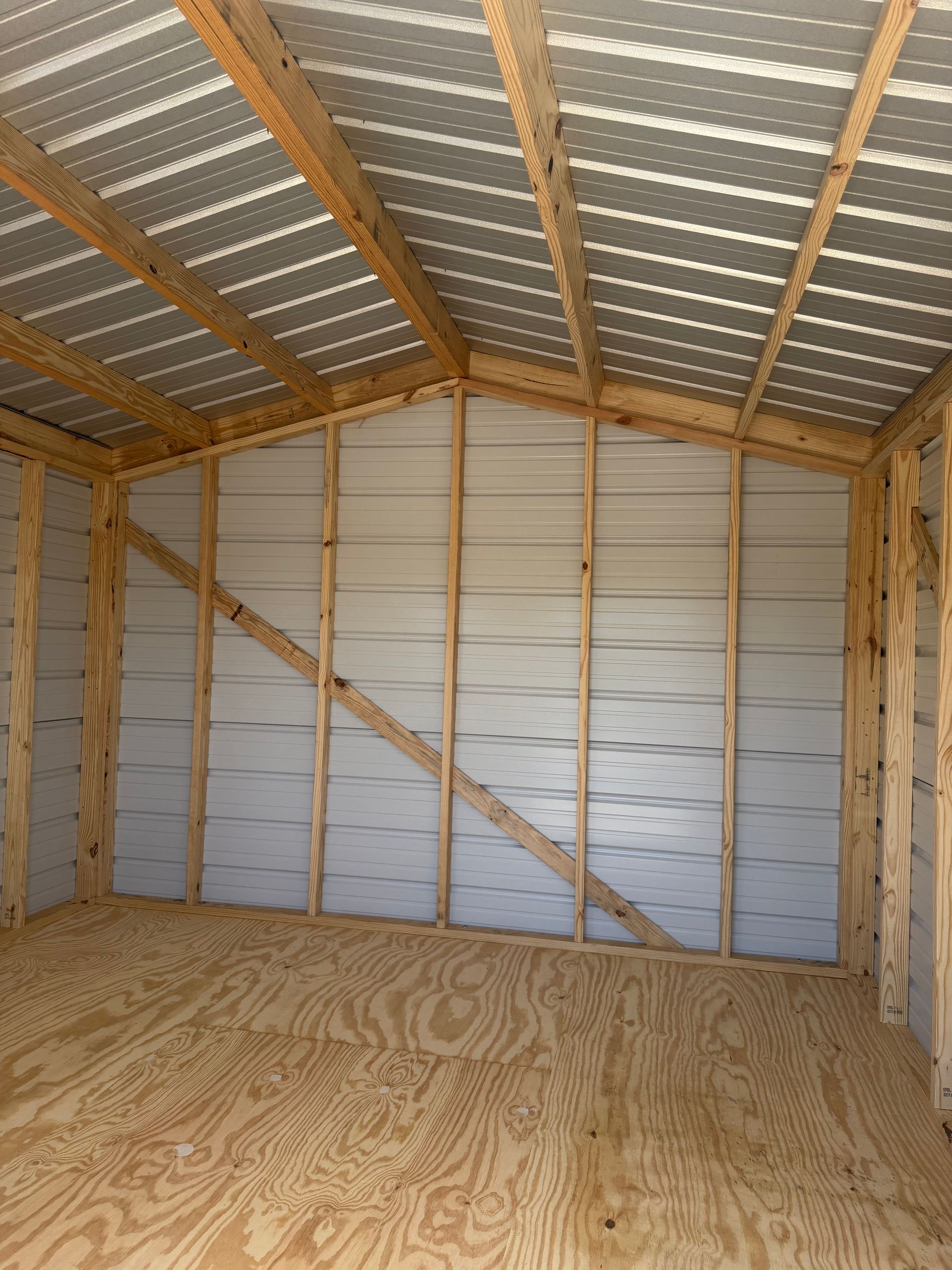 Empty unfinished shed interior with plywood floor, metal roof, and exposed wooden framing.