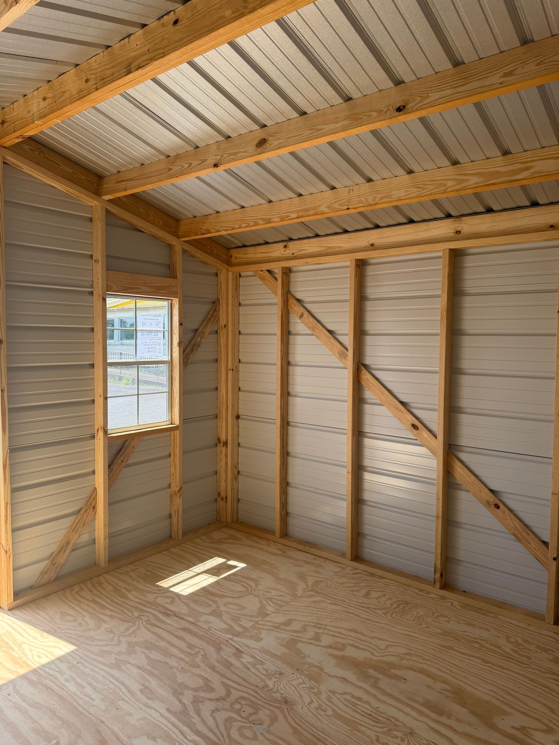 Empty unfinished room with plywood floor, exposed wood framing, insulated walls, and a small window.