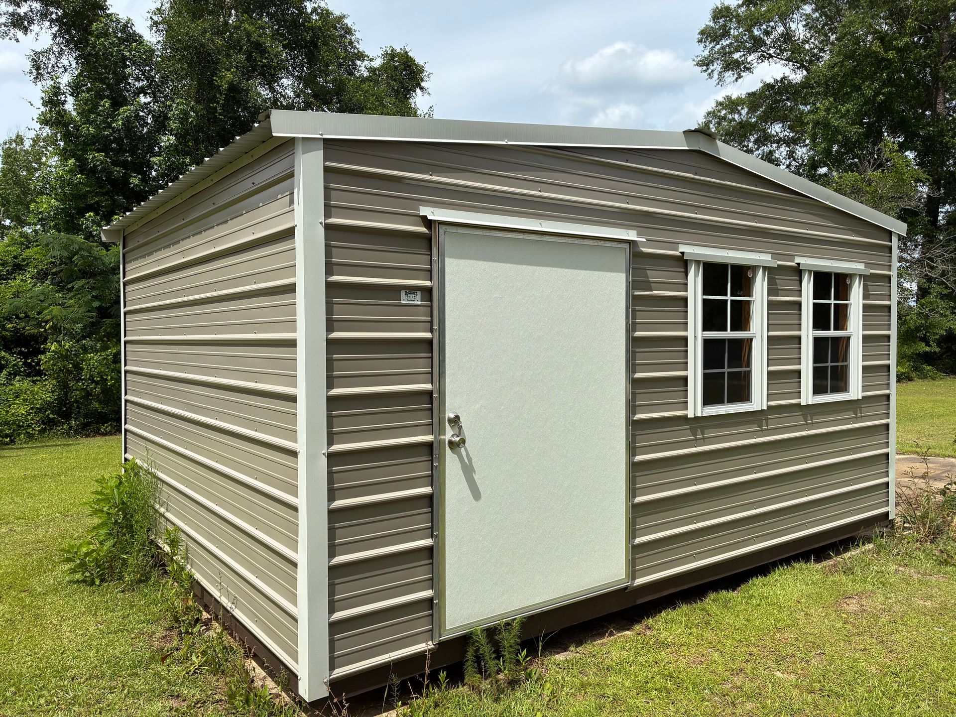 Small beige storage shed with white door and windows in a grassy yard