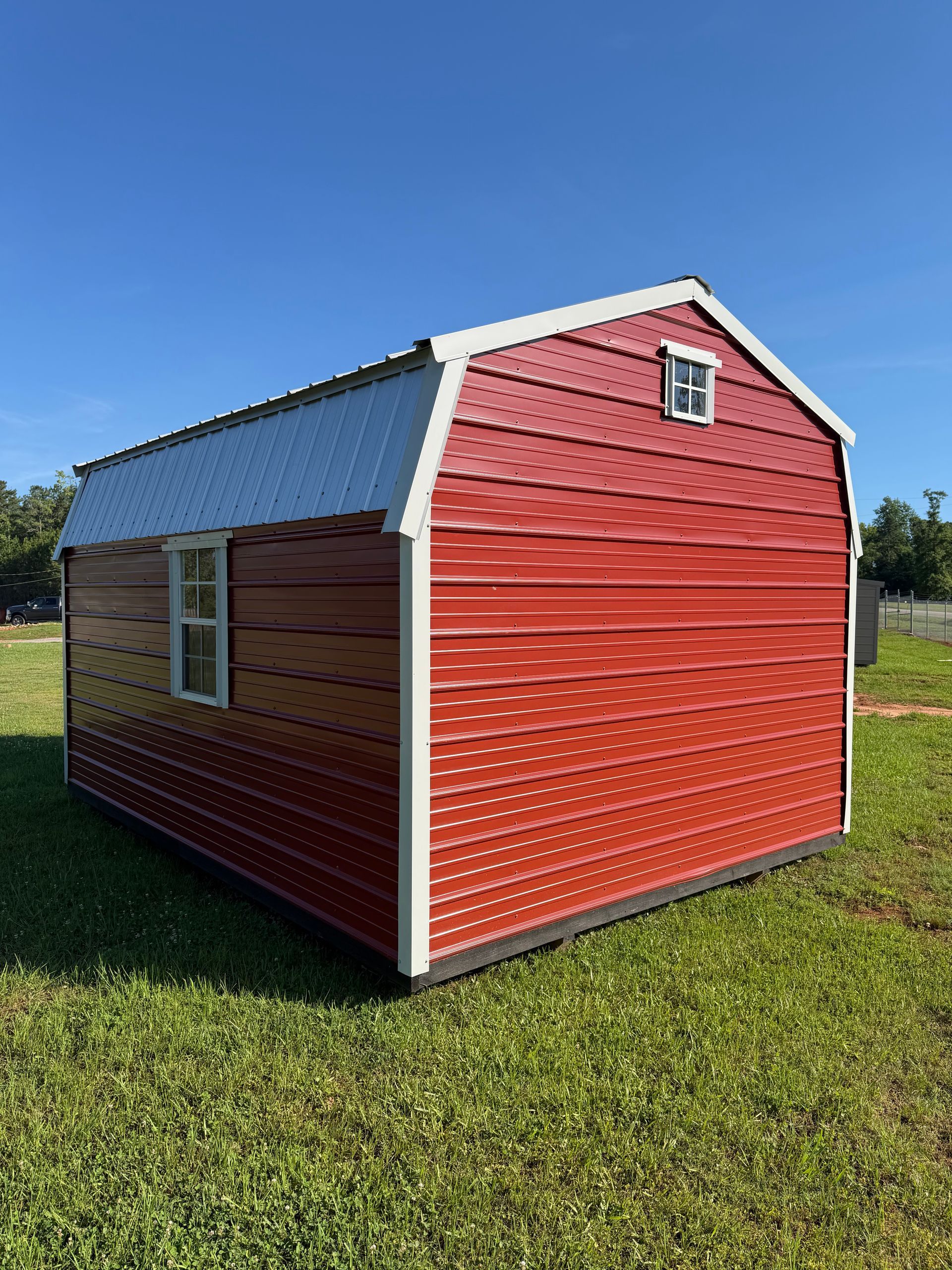 Red barn-style shed with white trim and a gray roof sitting on grass under a blue sky
