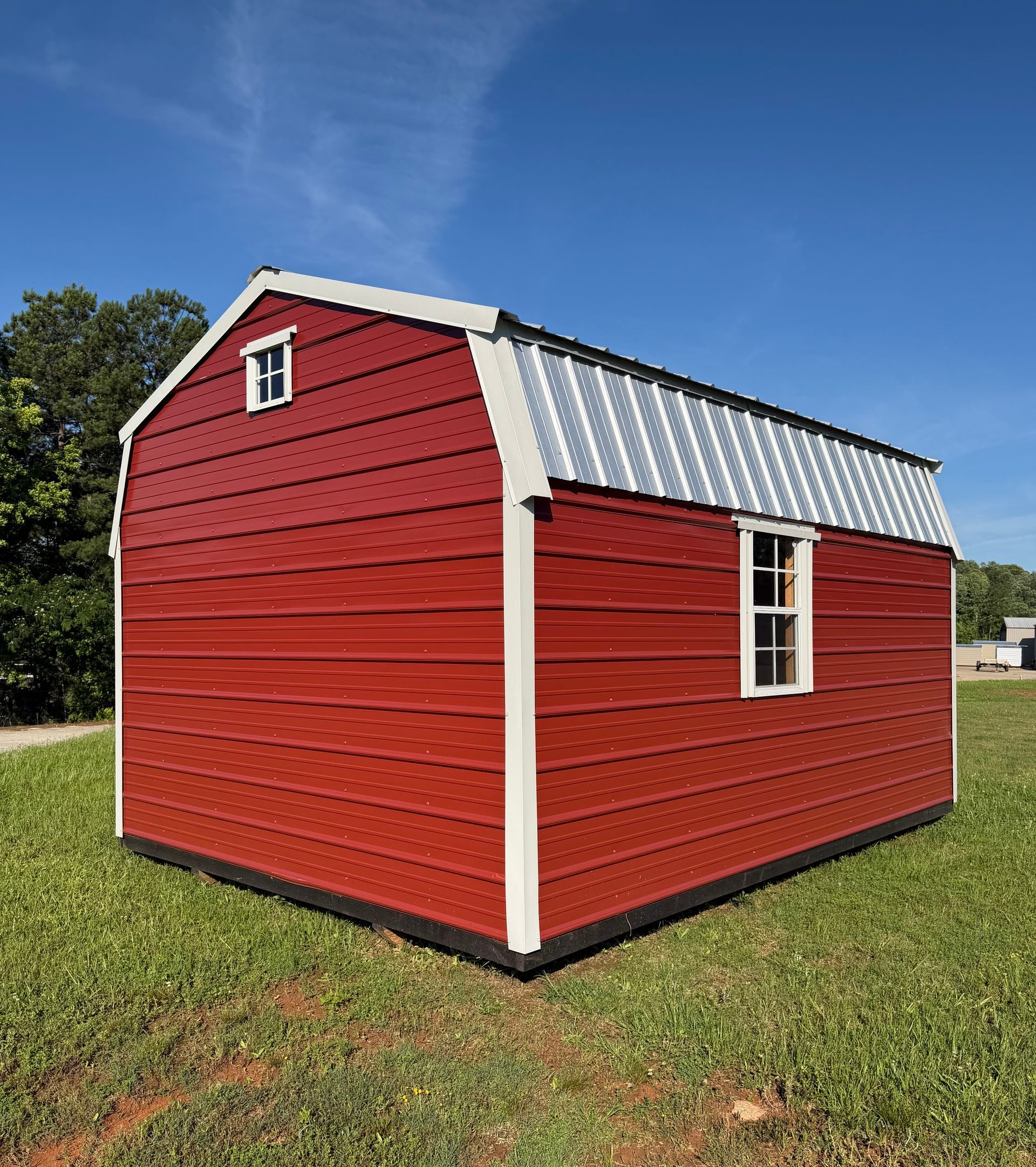 Red and white barn-style shed with a metal roof sitting on grass under a blue sky