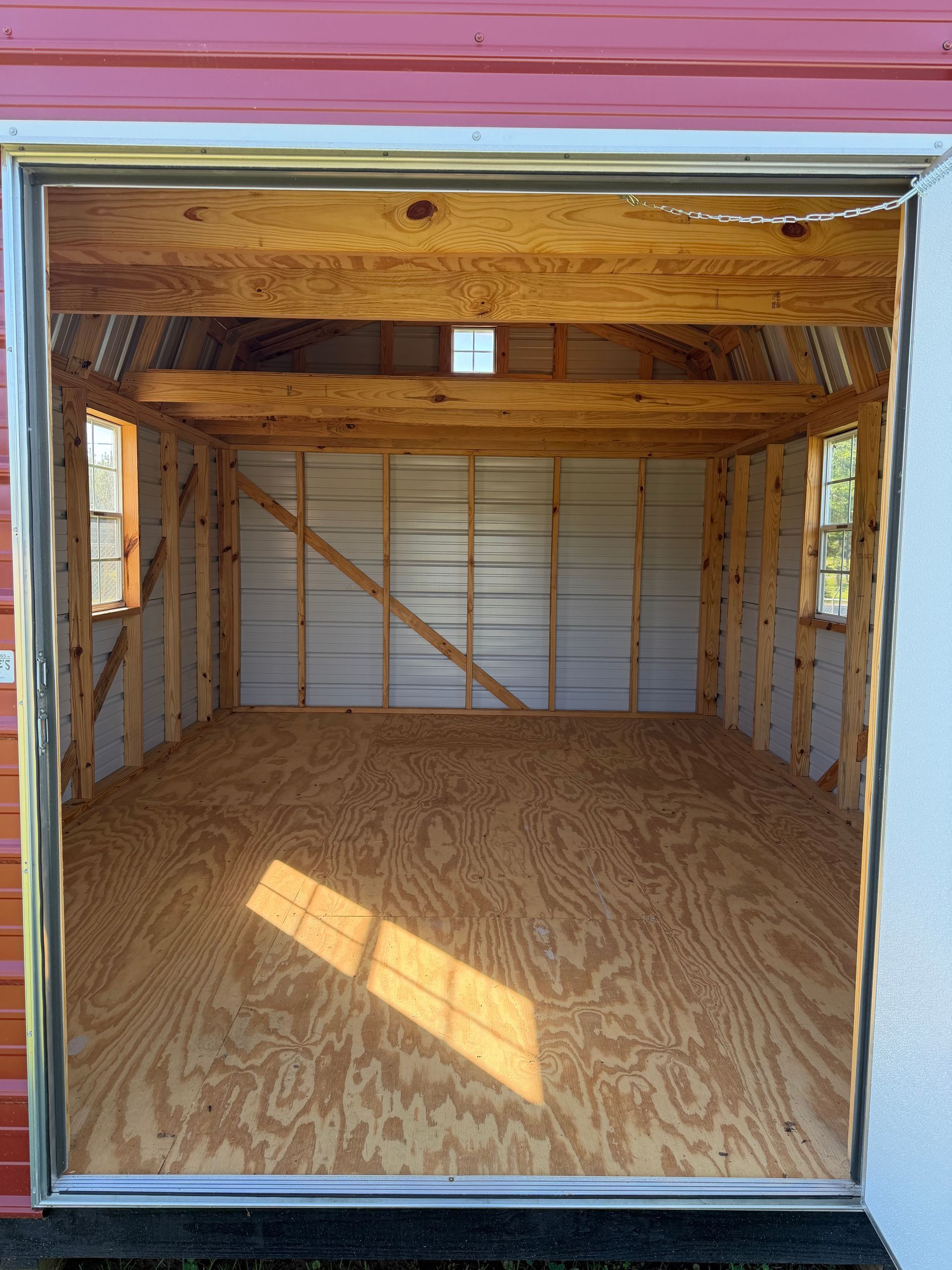 Empty wooden garage interior with open doorway, exposed beams, and plywood floor.