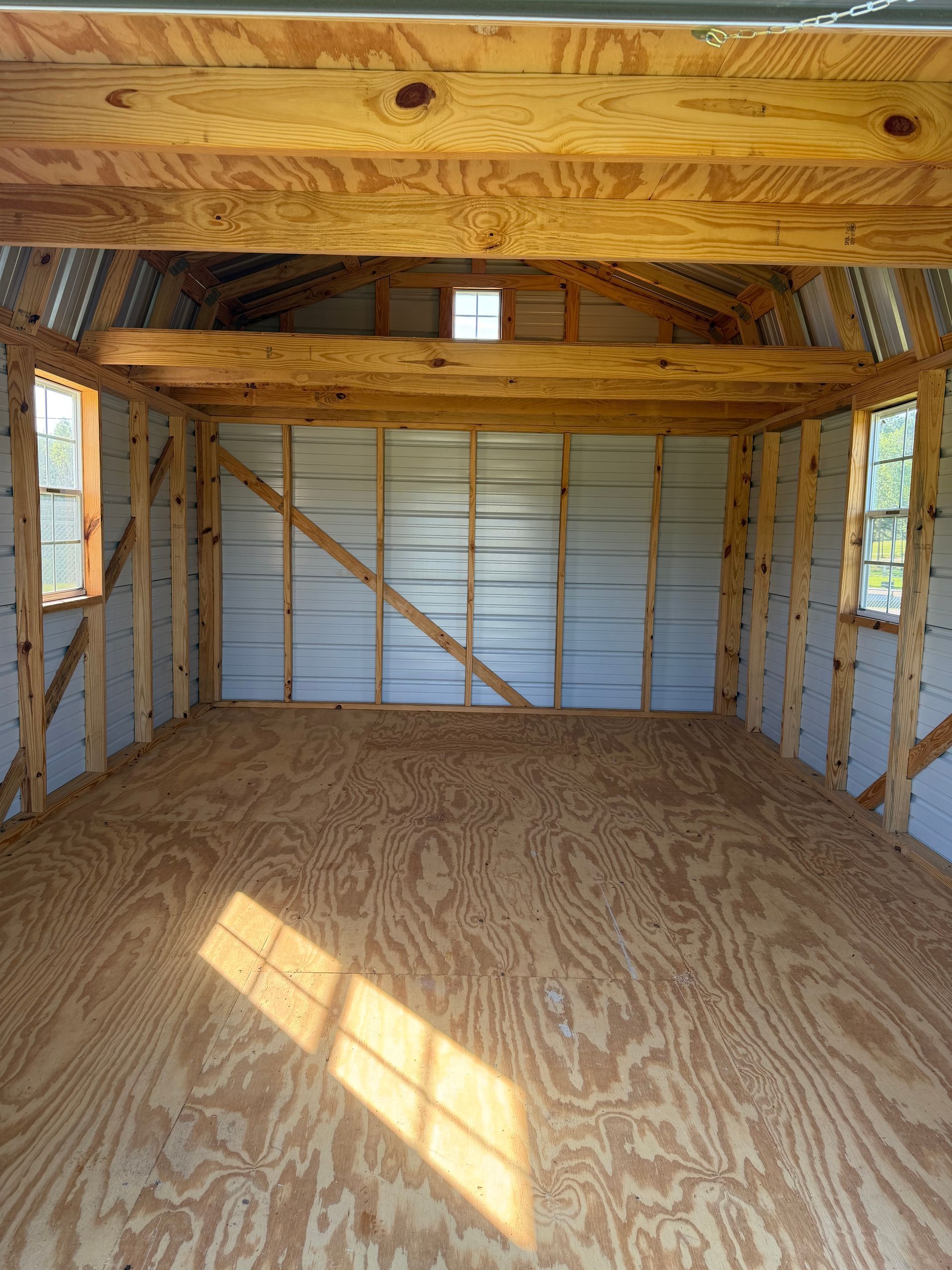 Empty unfinished wooden shed interior with plywood floor, exposed beams, and sunlight on the floor