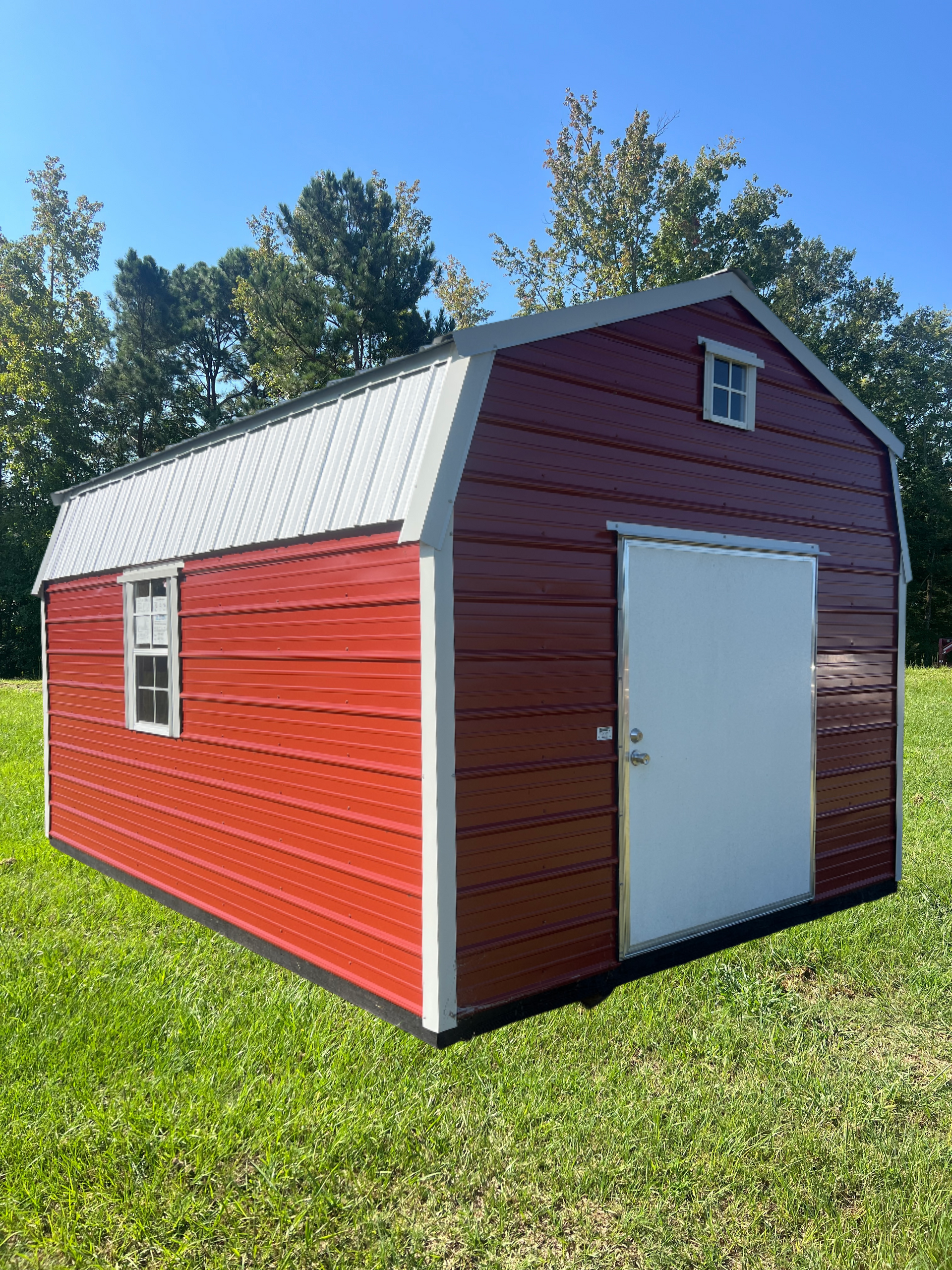 Red shed with white roof and door sitting on grass under a blue sky.