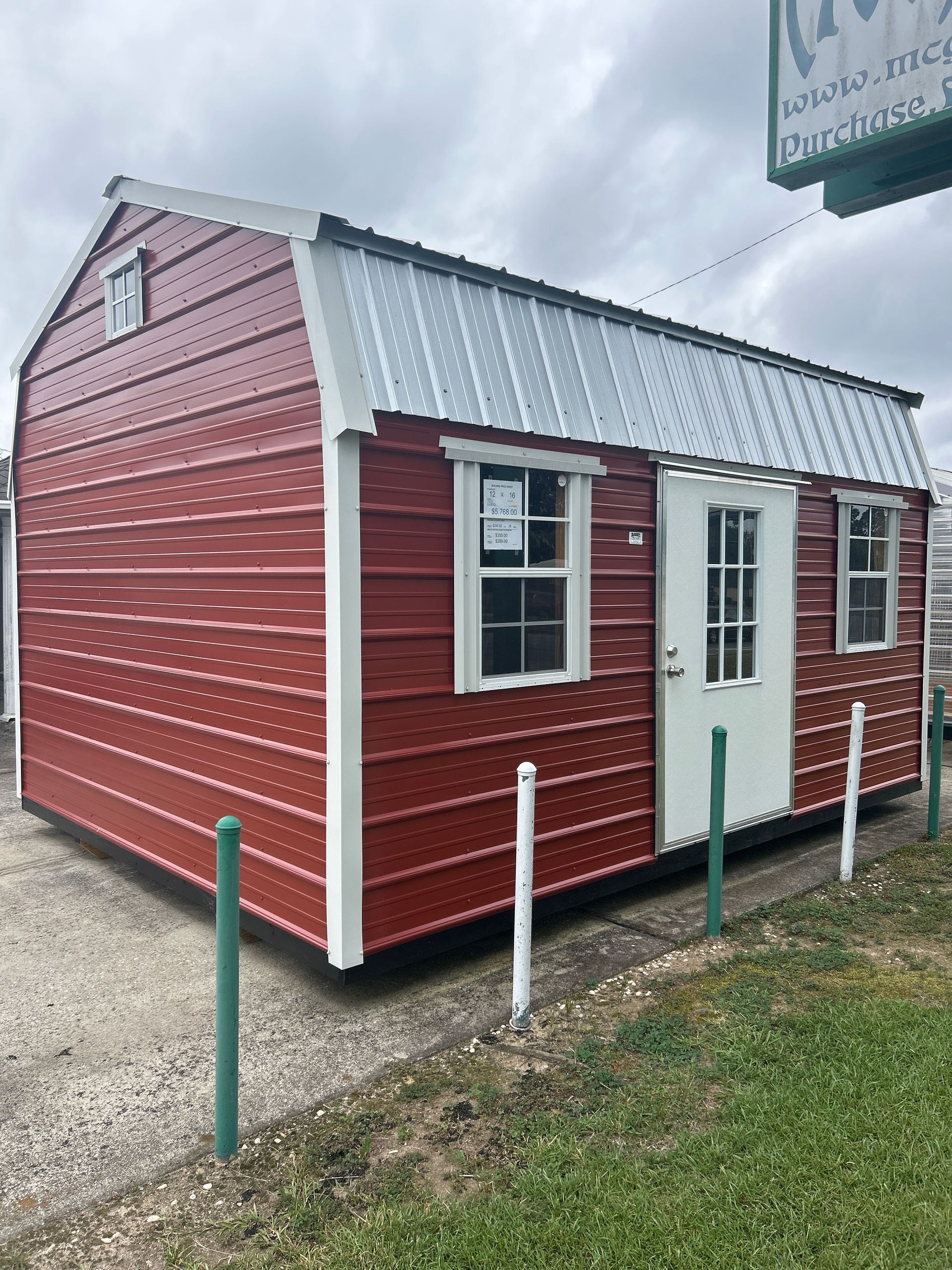 Small gray portable building with white roll-up door and window, sitting on gravel under a blue sky
