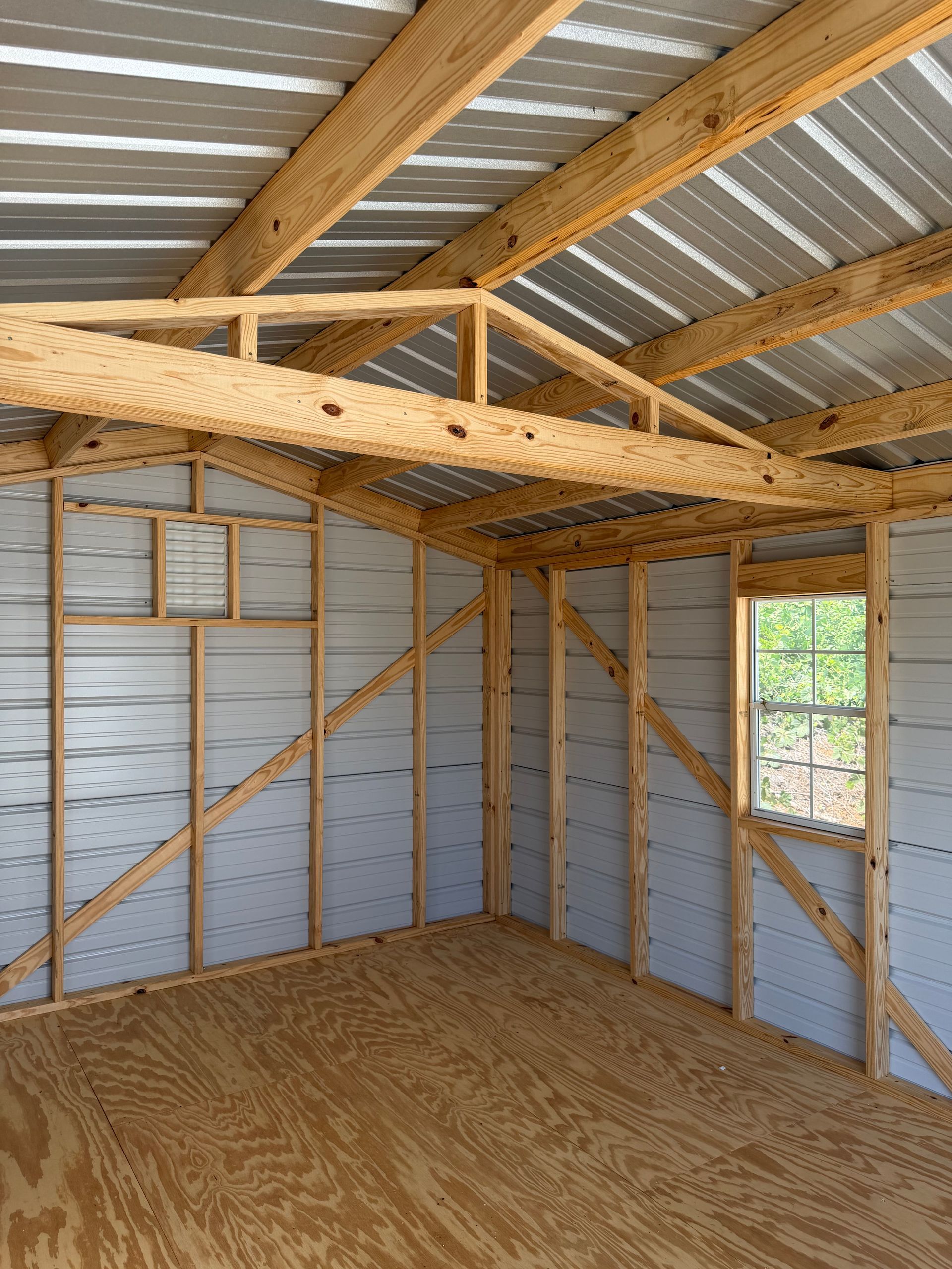 Interior of an unfinished shed with exposed wooden framing, metal roof, and plywood floor.