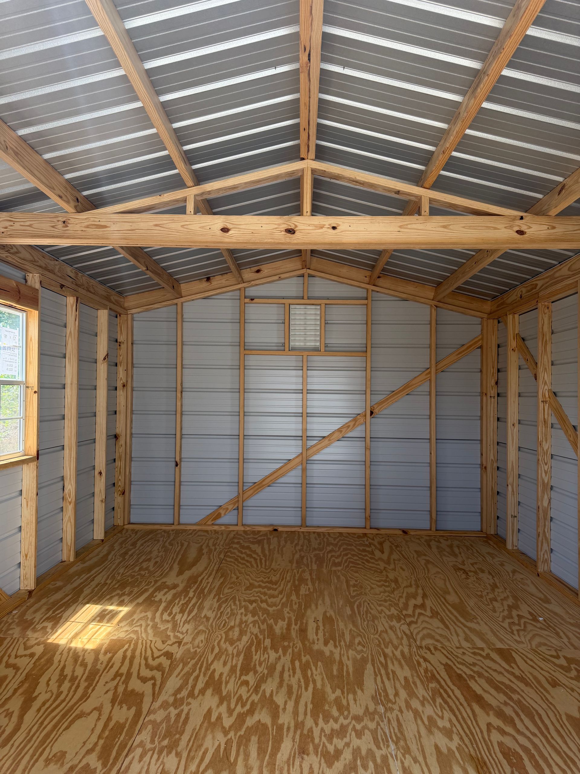 Empty unfinished shed interior with plywood floor, exposed framing, and corrugated metal walls and roof.
