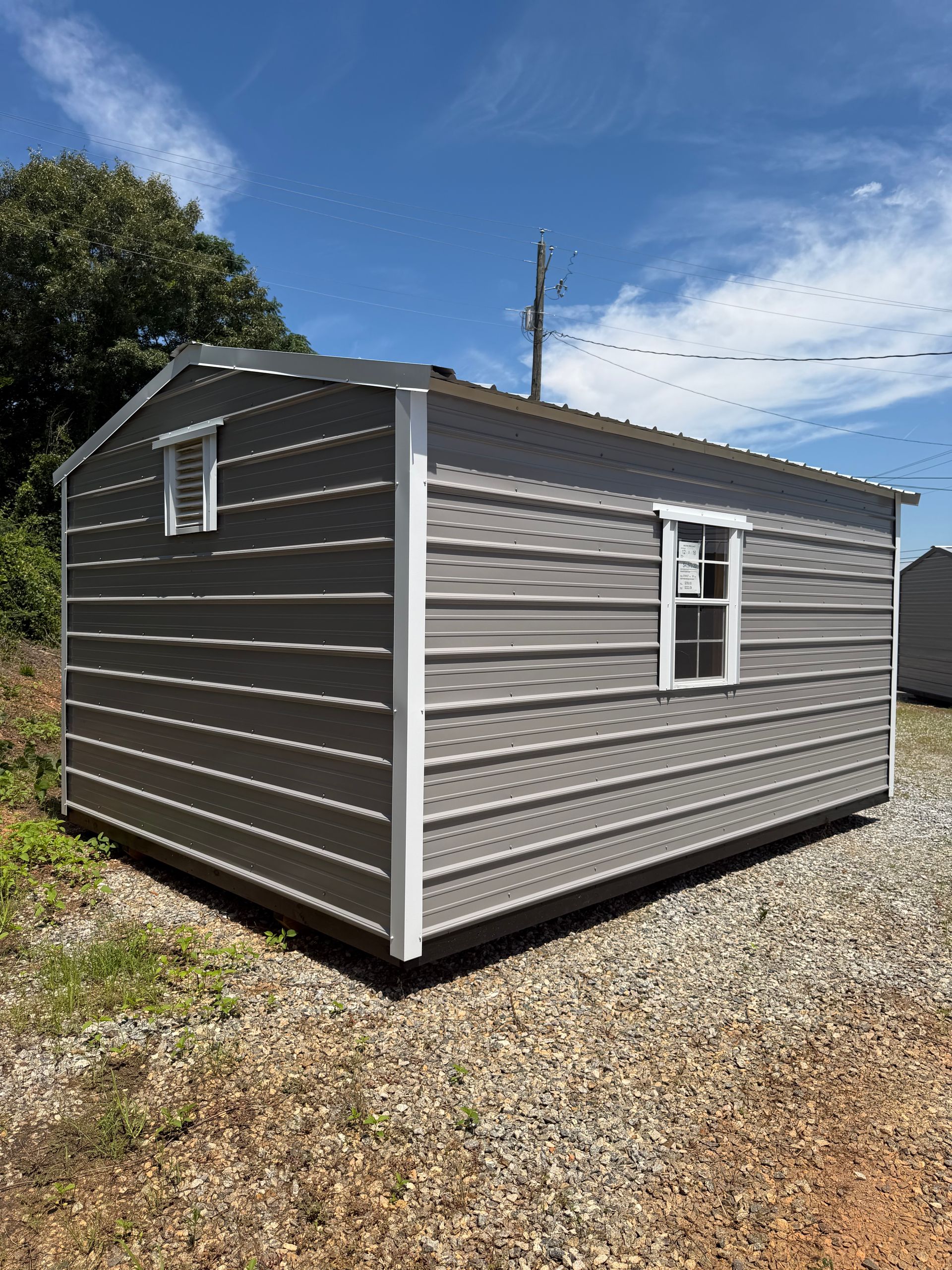 Gray portable shed with white trim on a gravel lot under a blue sky